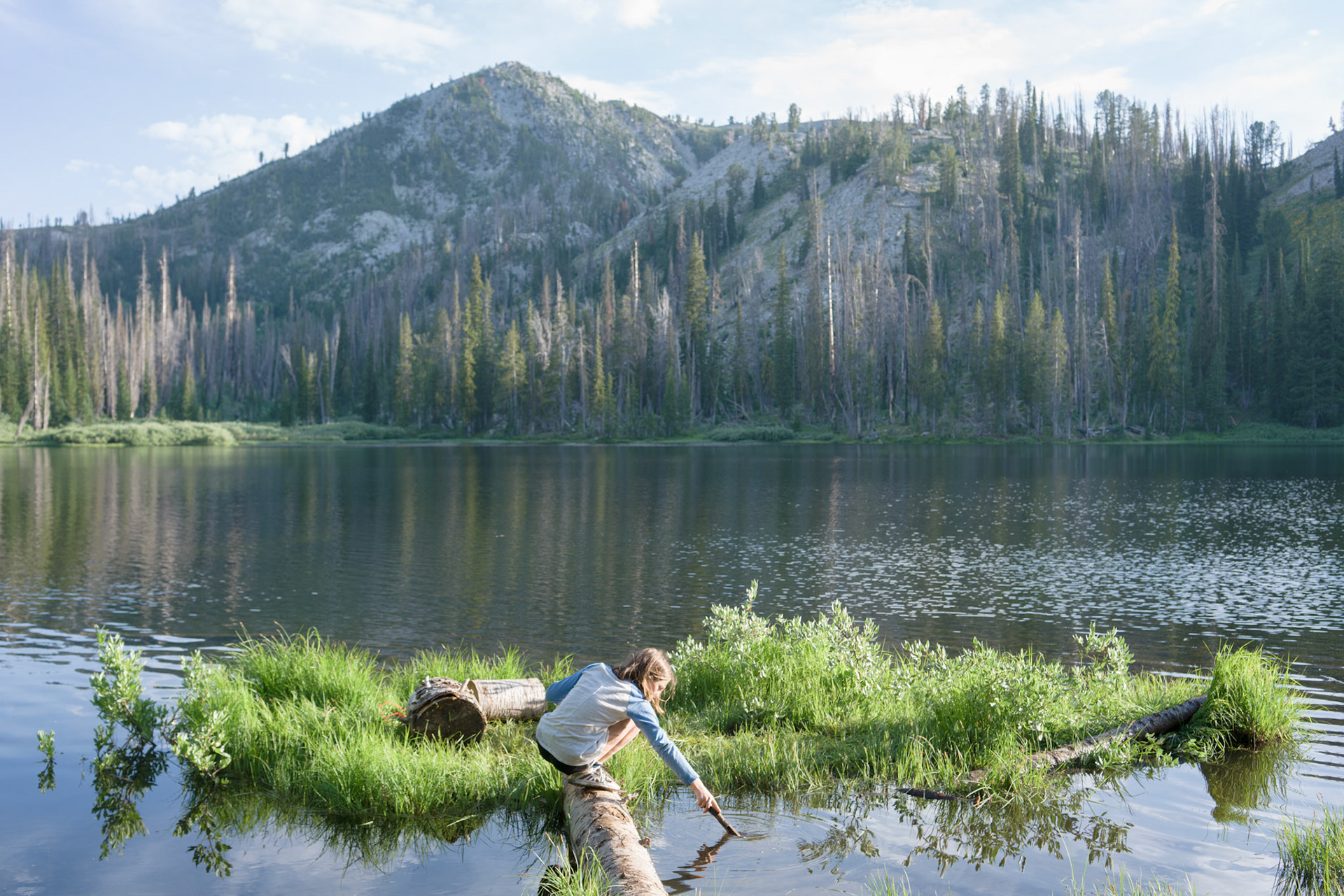 While I begin setting up our tent, Brenna goes straight to the shore where she finds a small log forming a bridge to a miniature, grass covered island. She crosses then sets to work creating another little bridge to a further island.“Those are your only shoes,” I call out to remind her. “Don’t get them wet.”