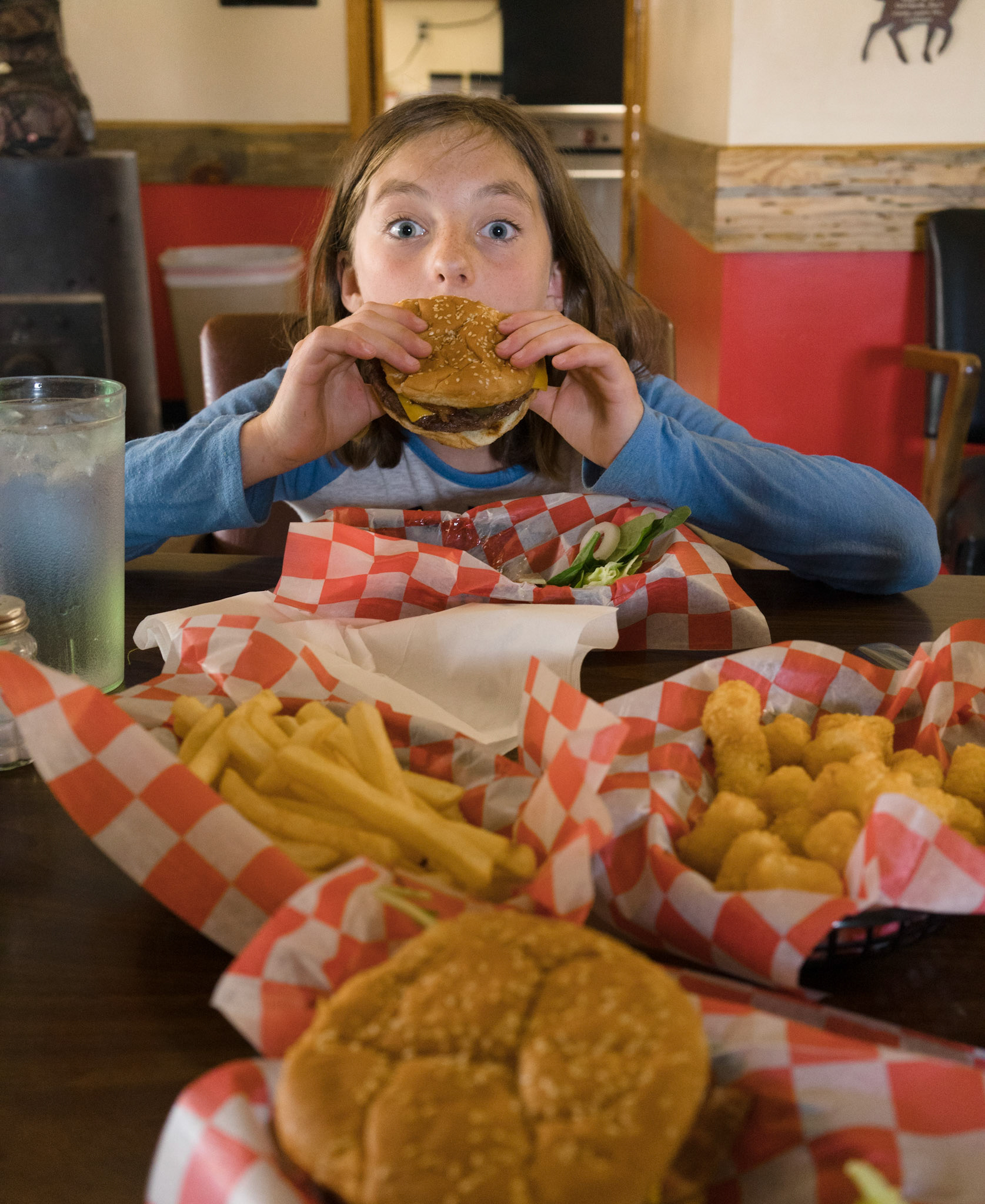 The ride isn’t so much about riding as the experiences along the way. And this being Brenna’s first big ride, we’ll take several breaks to keep it comfortable.We last ate together at the Prairie Y-Stop about one year ago with our French exchange student Alexis.¹ “Do you remember eating here?” I ask after we come to a stop in the dirt lot aside the corrugated blue metal building.“Yeah,” Brenna answers.We walk in past store shelves to the restaurant in the back and find the lone proprietor, a grizzled man, tapping away on an old laptop. He hops cheerfully to his feet and hands us menus before disappearing into the kitchen to ready the grill.“He was singing while you were in the bathroom,” Brenna tells me under her breath when I return to our table from rinsing off ATV dust.“That’s good,” I suggest. “I’m glad he’s happy!”___¹ Trail Image, “Fathers Day Prairie Loop”: https://www.trailimage.com/fathers-day-prairie-loop