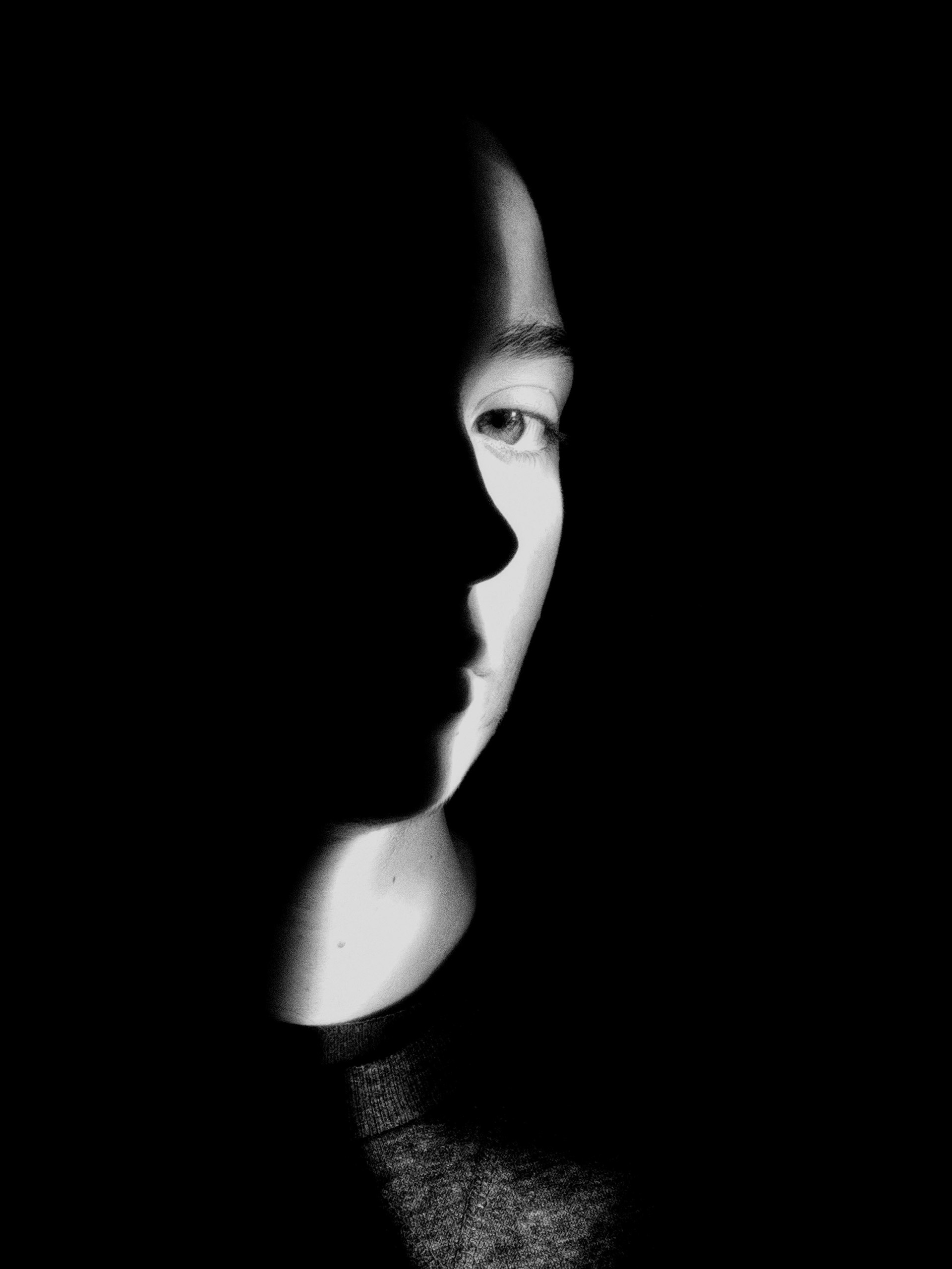 Black and white portrait photography . Half the models face is shrouded in shadow. The shadow outlines her profile.