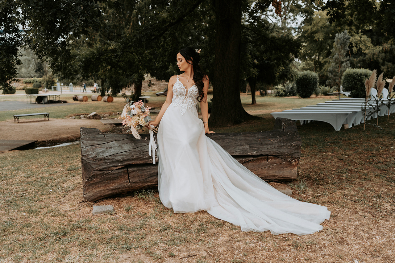 Braut alleine mit Brautstrauß auf einem Baumstumpf mit Blick nach unten
