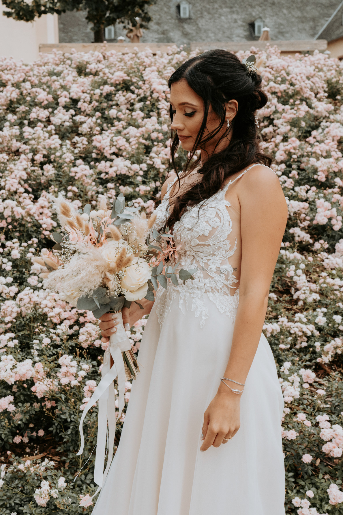 Hübsche Braut mit vielen rosa Blumen im Hintergrund