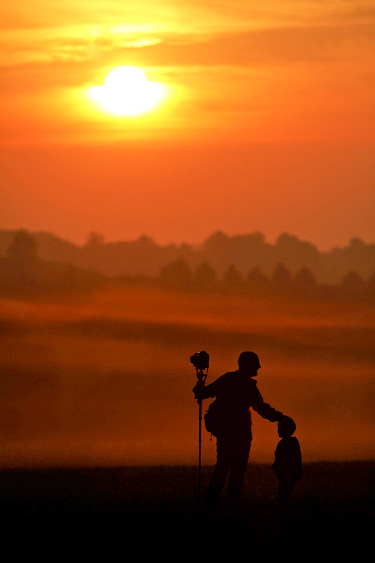 A photographer and his son watch the sunrise shortly before the kickoff of the Midwest Balloon Festival in Overland Park, Kansas.