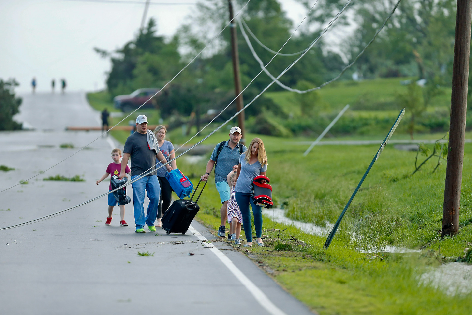 A family ducks under power lines as they make their way out of a tornado damaged neighborhood after being hit on Tuesday, May 28, 2019, south of Lawrence, Kan., near US-59 highway and N. 1000 Road. [Chris Neal/The Capital-Journal]