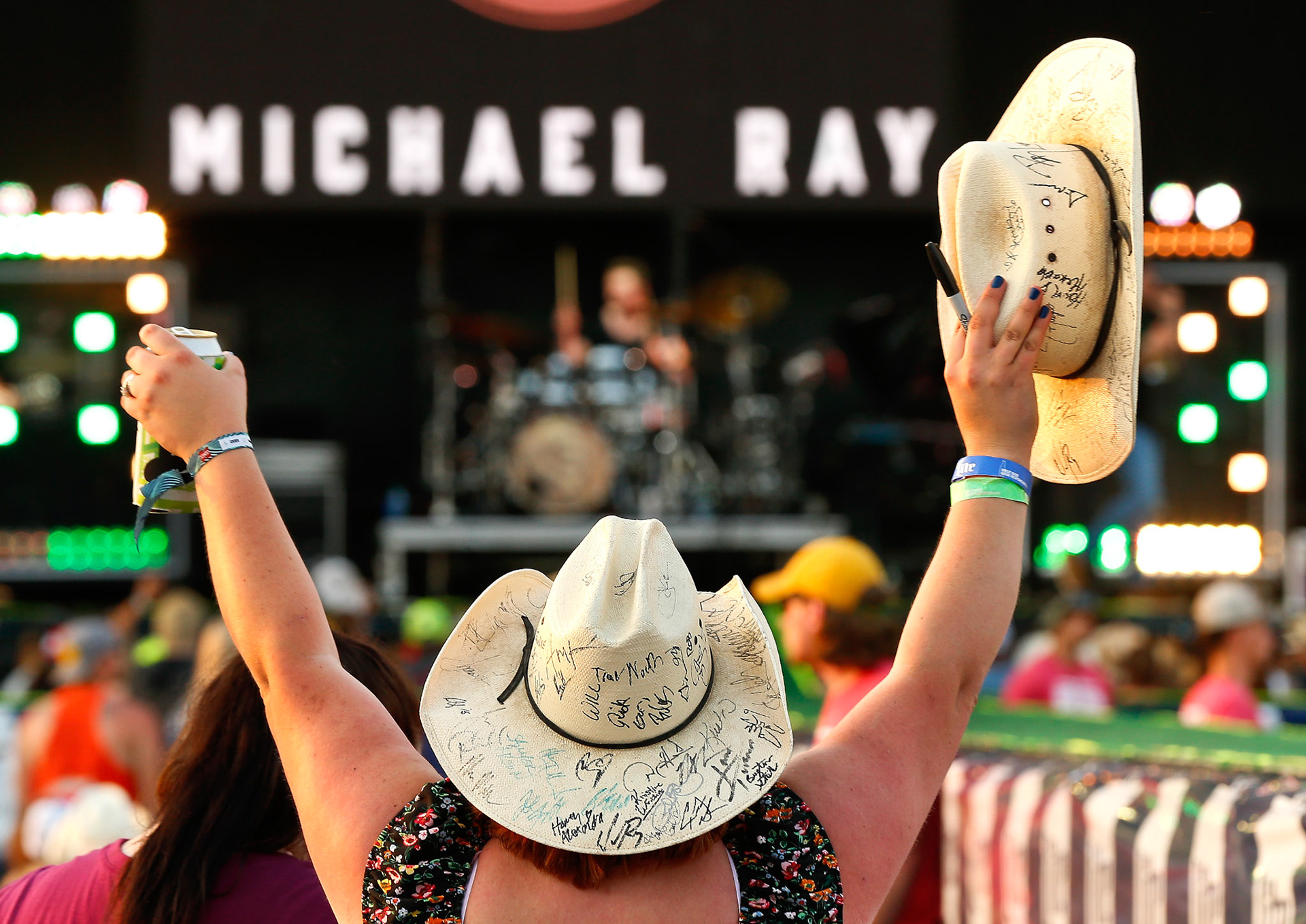 With a beer in one hand and an autographed cowboy hat in the other, a country music fans raises her hands in the air as Michael Ray takes the stage at Friday's Kicker Country Stampede at Heartland Motorsports Park. [Chris Neal/The Capital-Journal]