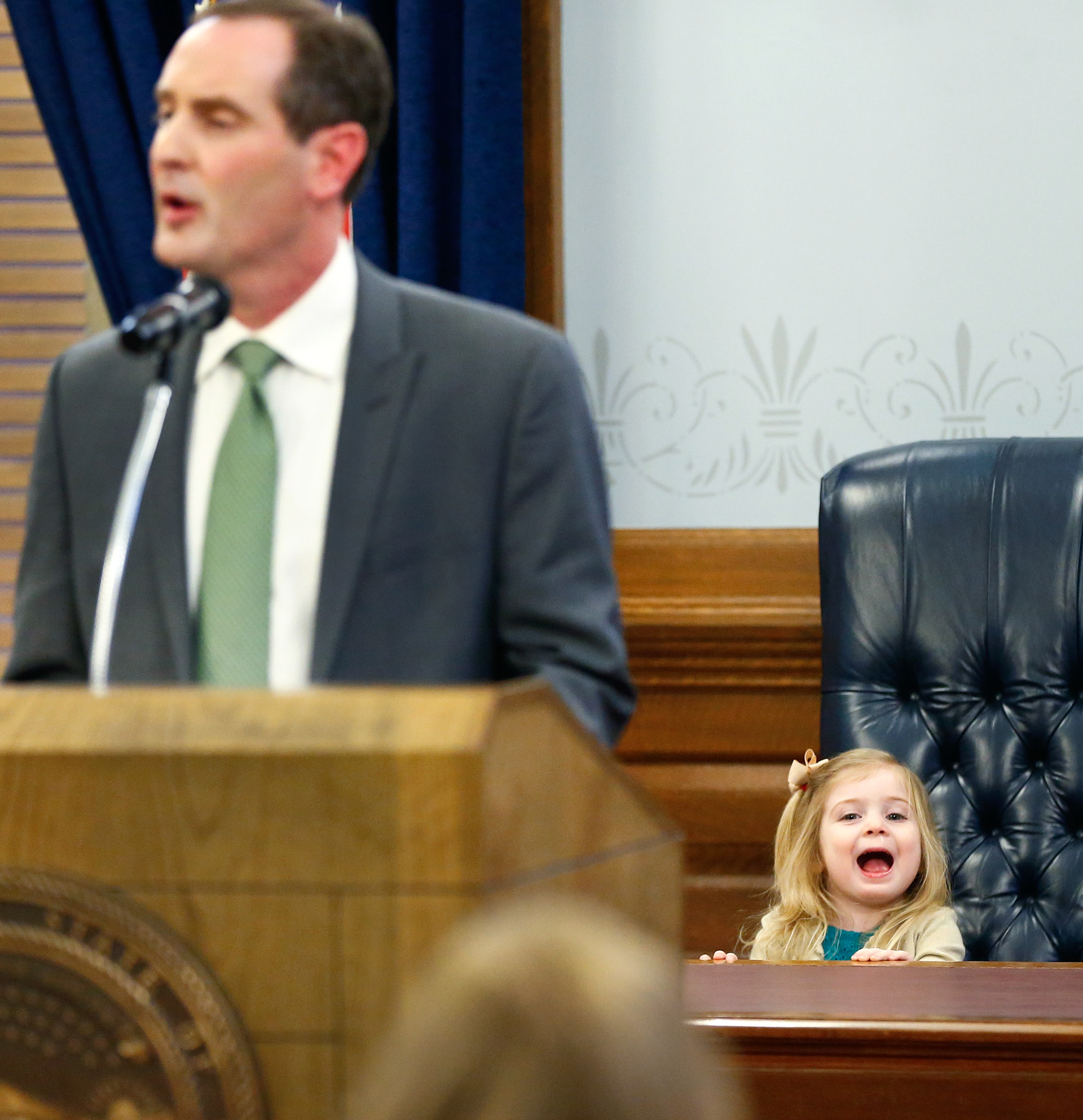 Tracey Mann's 2-year-old daughter Whitney sits at the desk inside the Kansas Statehouse's ceremonial office while her father addresses a large crowd after being sworn in as the new Lieutenant Governor of Kansas on Wednesday, Feb. 14, 2018, at the Kansas Statehouse in Topeka, Kan. [Chris Neal/The Capital-Journal]
