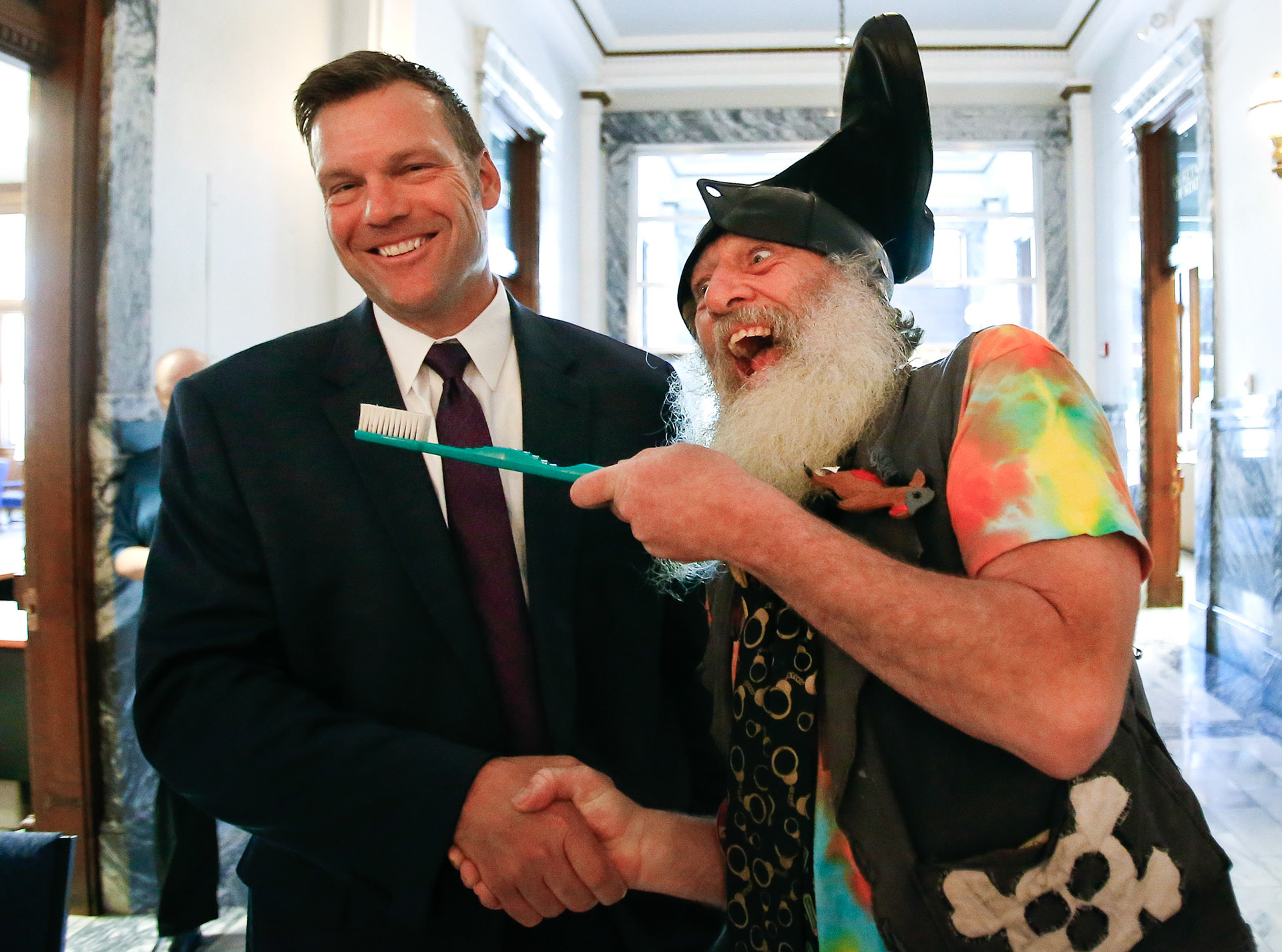 Vermin Supreme greets Kansas Secretary of State Kris Kobach with a handshake and an oversized toothbrush after filing as candidate for Kansas attorney general on Friday, June 1, 2018, at  Memorial Hall in downtown Topeka, Kan. [Chris Neal/The Capital-Journal]