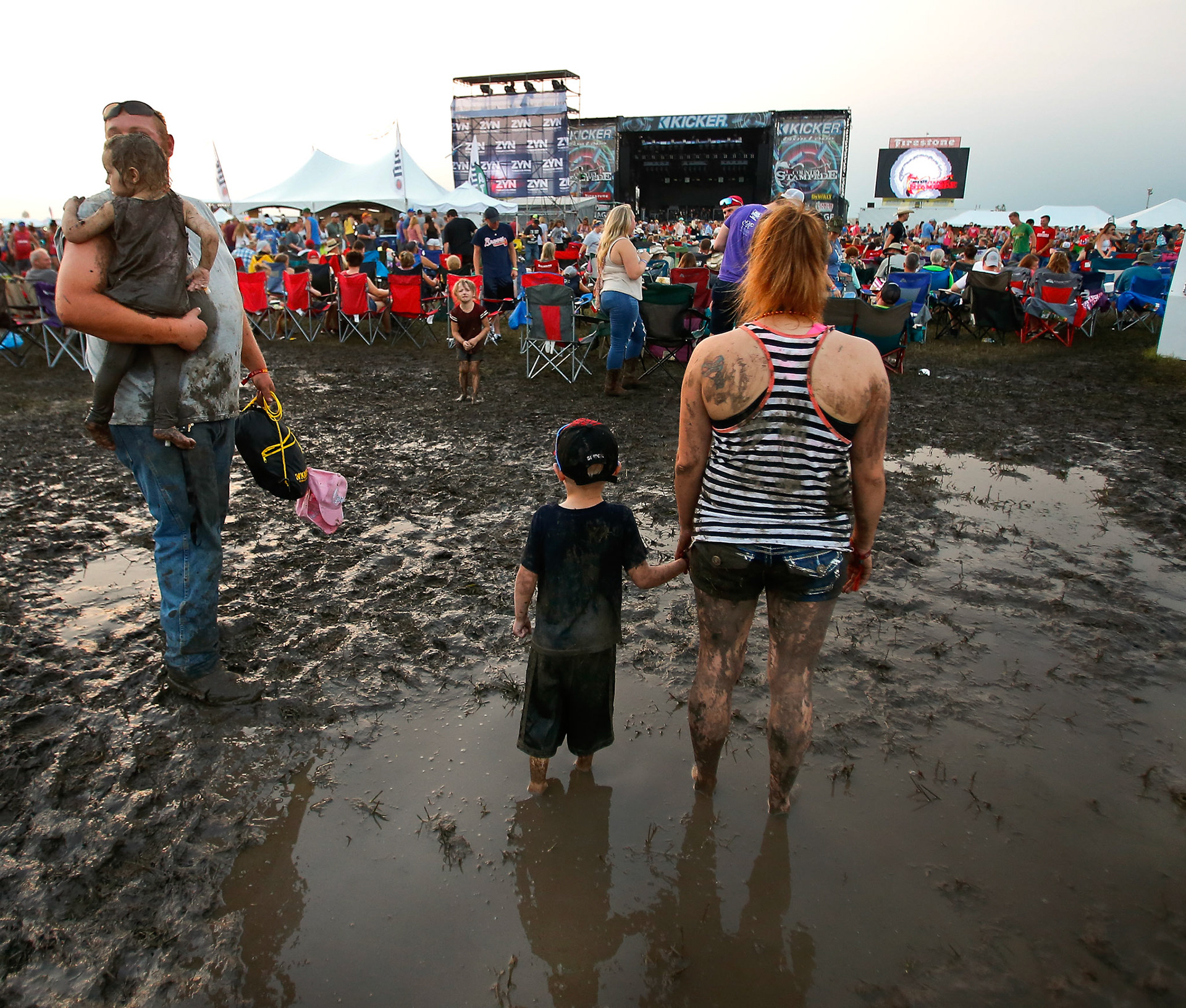 While waiting for Old Dominion to take the stage, a family stands in a mud puddle in the festival grounds at Friday's Kicker Country Stampede at Heartland Motorsports Park. [Chris Neal/The Capital-Journal]