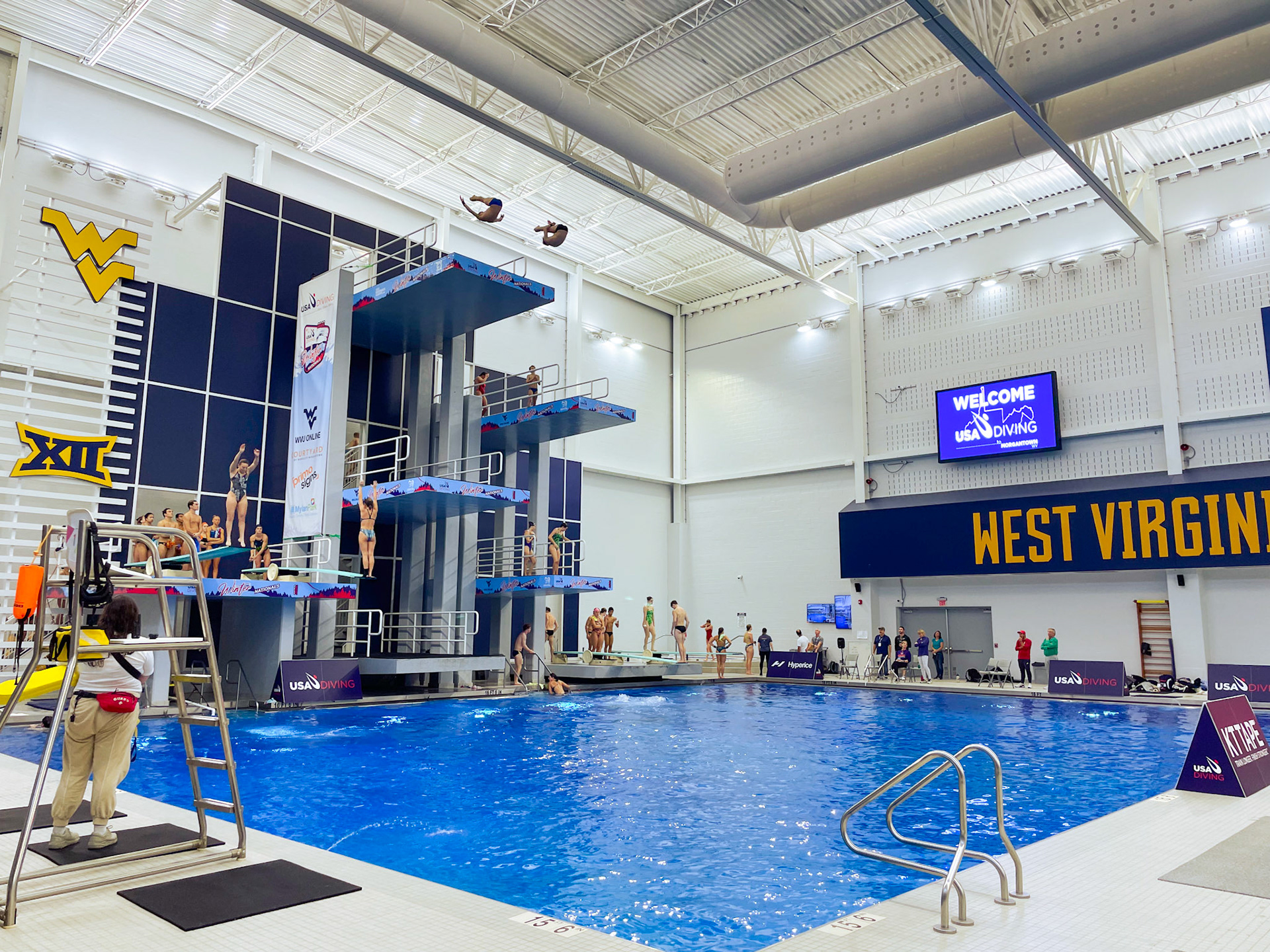 Banner and Platform Wrap Designs on The Aquatic Center at Mylan Park Dive Well and Diving Tower Front Angled View with Synchronized Diver Mid Somersault