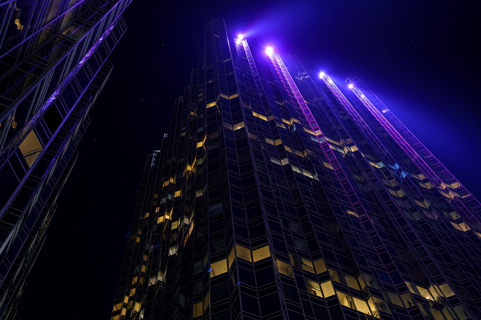 Dramatic night scene of skyscraper looking up with purple rays of light by Ryan Bucchianeri.