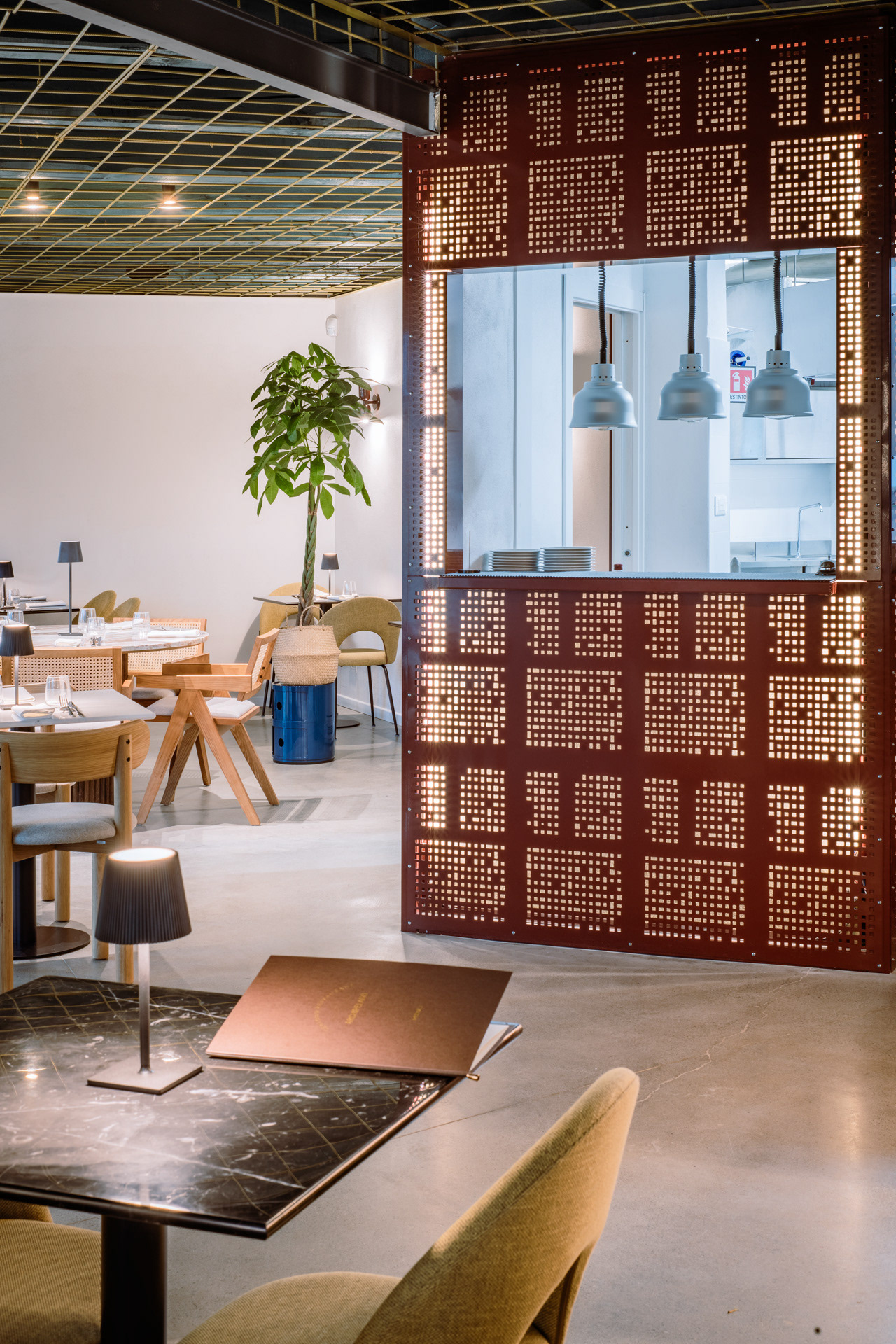 Altra vista dell'interno del ristorante Archipelago con griglia metallica forata retroilluminata. Cucina aperta verso ristorante con passa vivande raffinato.