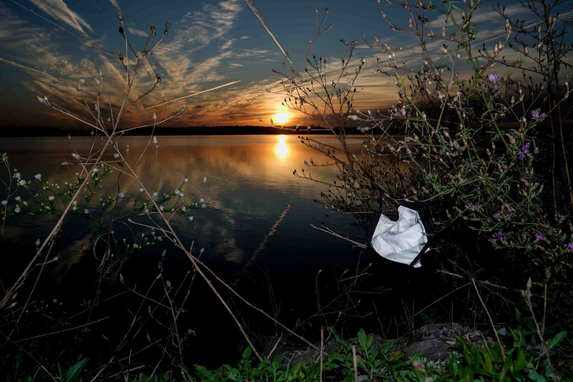 A discarded mask hangs off shrubs lining Onondaga Lake outside of the Honeywell Visitors Center in Syracuse, New York on Wednesday, September 30. The Center marks the location of the Onondaga lake boat launch and remains littered with garbage years after the restoration of the lake was complete.