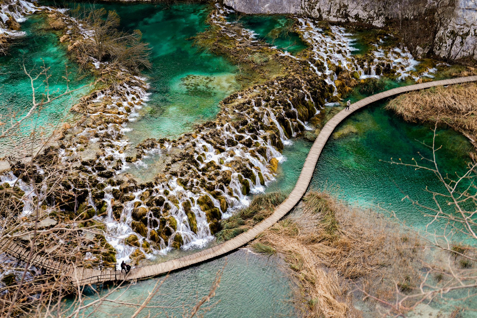 Tourists cross the wooden paths of Plitvička National Park, where cascading waterfalls and clear lakes now draw visitors from around the world—an image of tranquility far from the conflict that once defined Croatia.