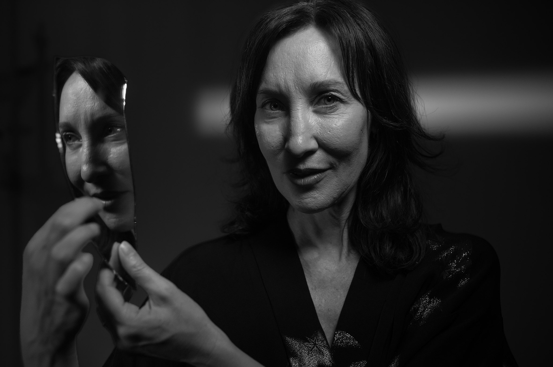 Portrait en noir et blanc : une femme tient un miroir où se reflète son visage.