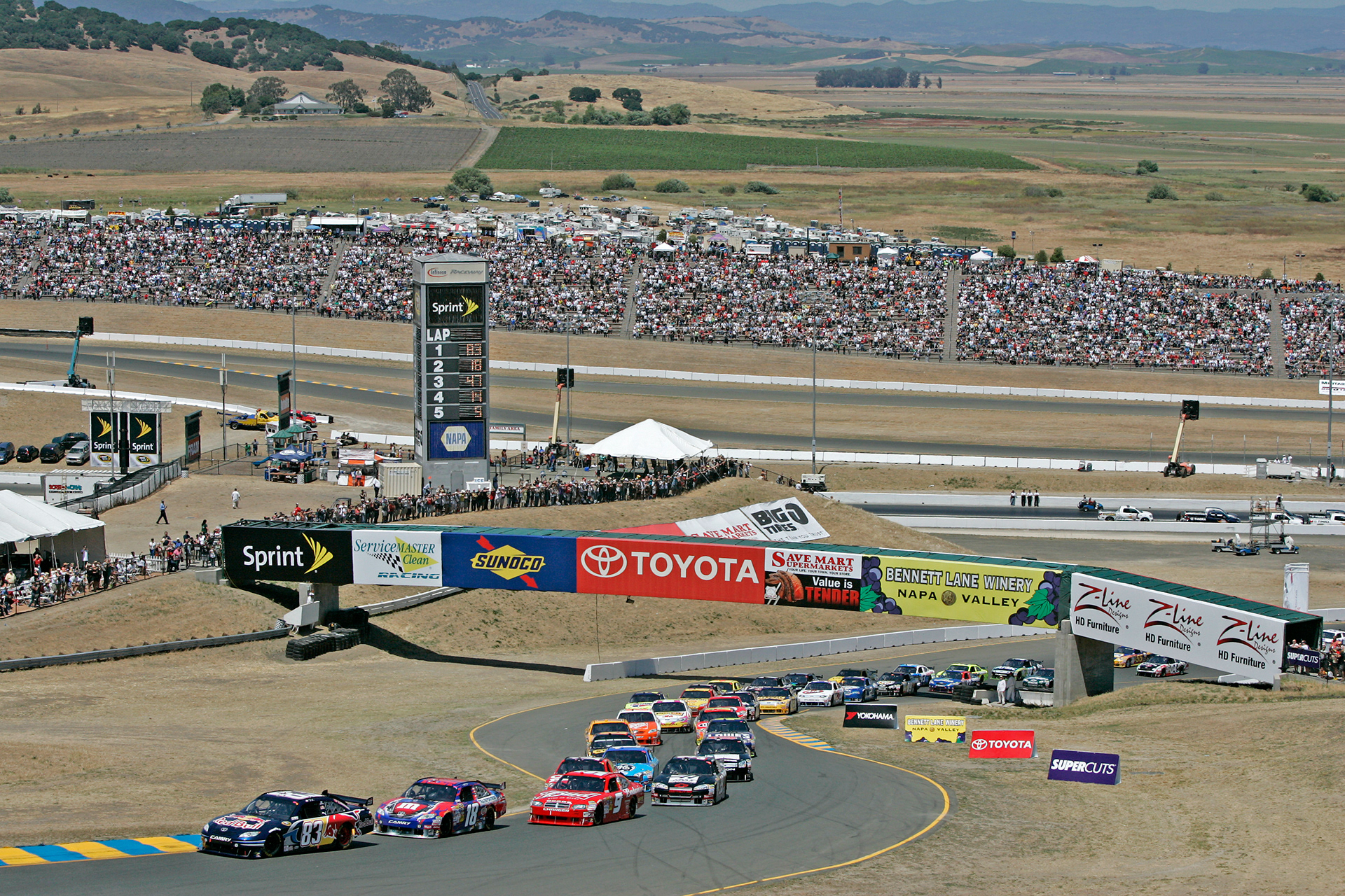 The #83 Red Bull car leads a crowded NASCAR restart at Sonoma.  ©  IAN DONALD