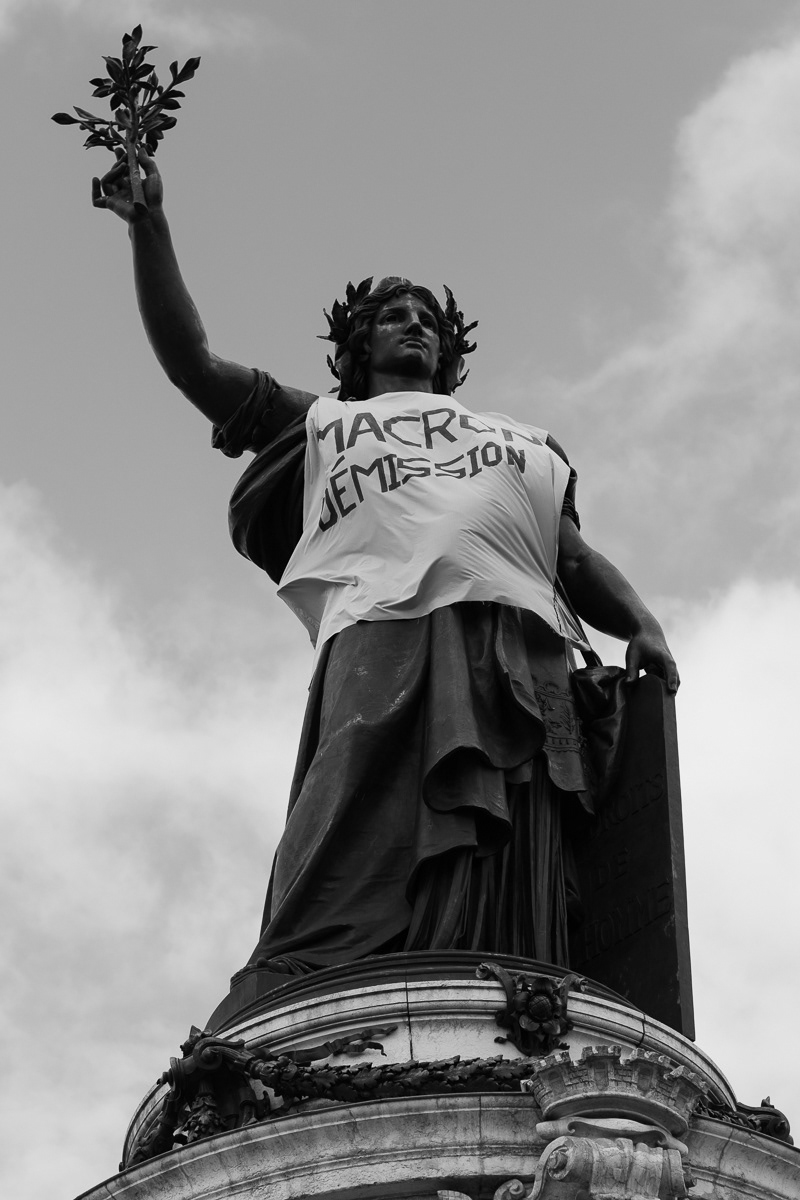 Statue with yellow vest, holding inscription claiming President Macron resignation, May 2023, Paris