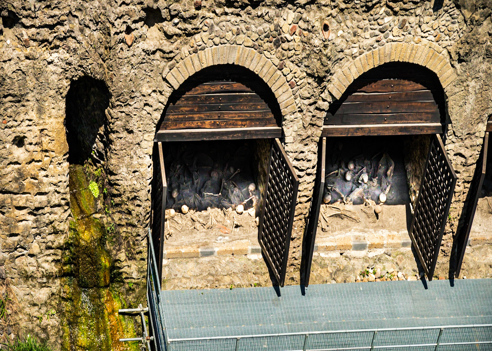Arched chambers—possibly boathouses or warehouses—where human skeletons were found during excavations at Herculaneum.  They can still be seen in the positions they died that day.