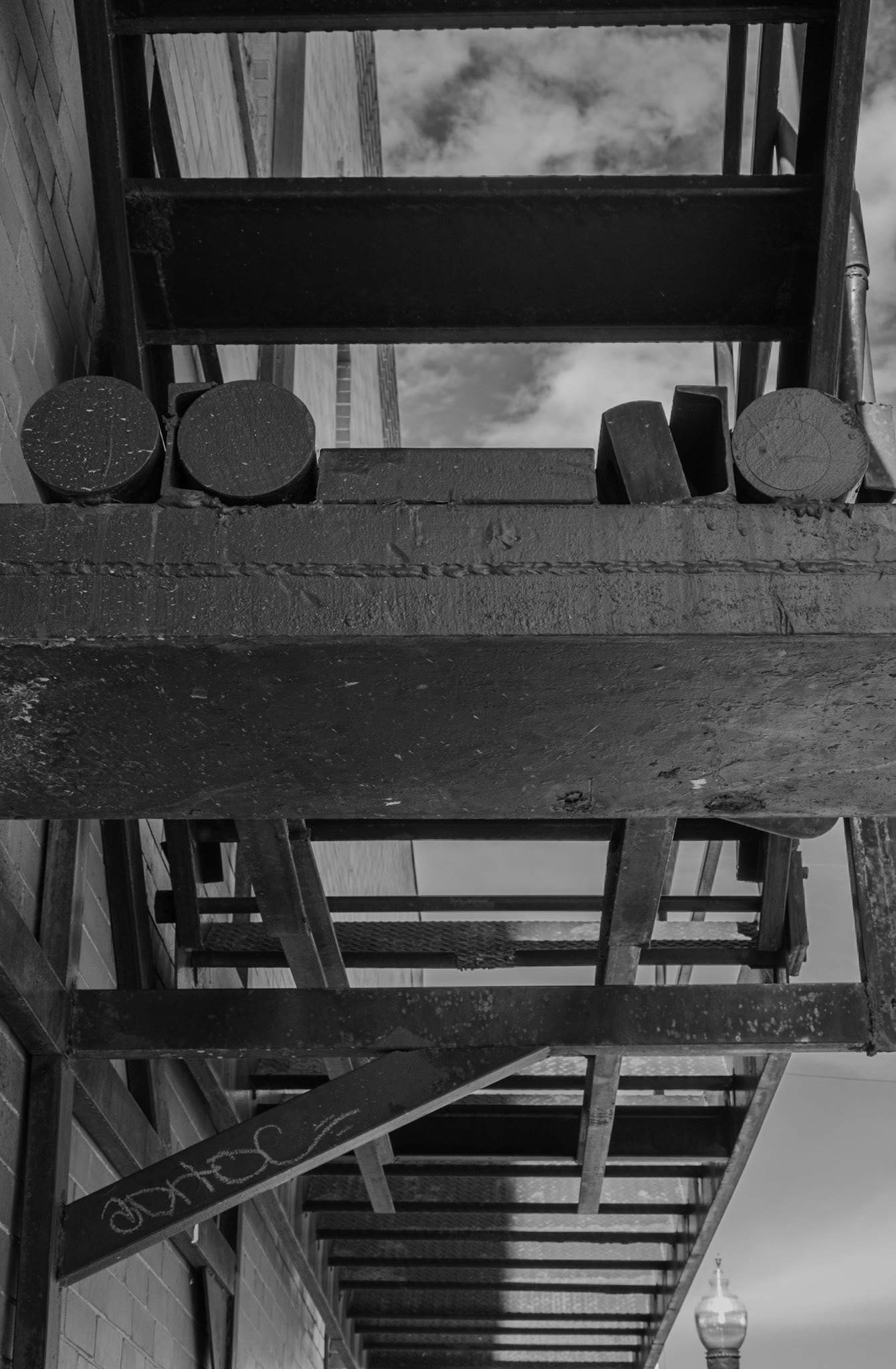 Black and white photograph capturing the intricate metal structure of an industrial fire escape against a clear sky, highlighting urban architecture and geometric patterns.