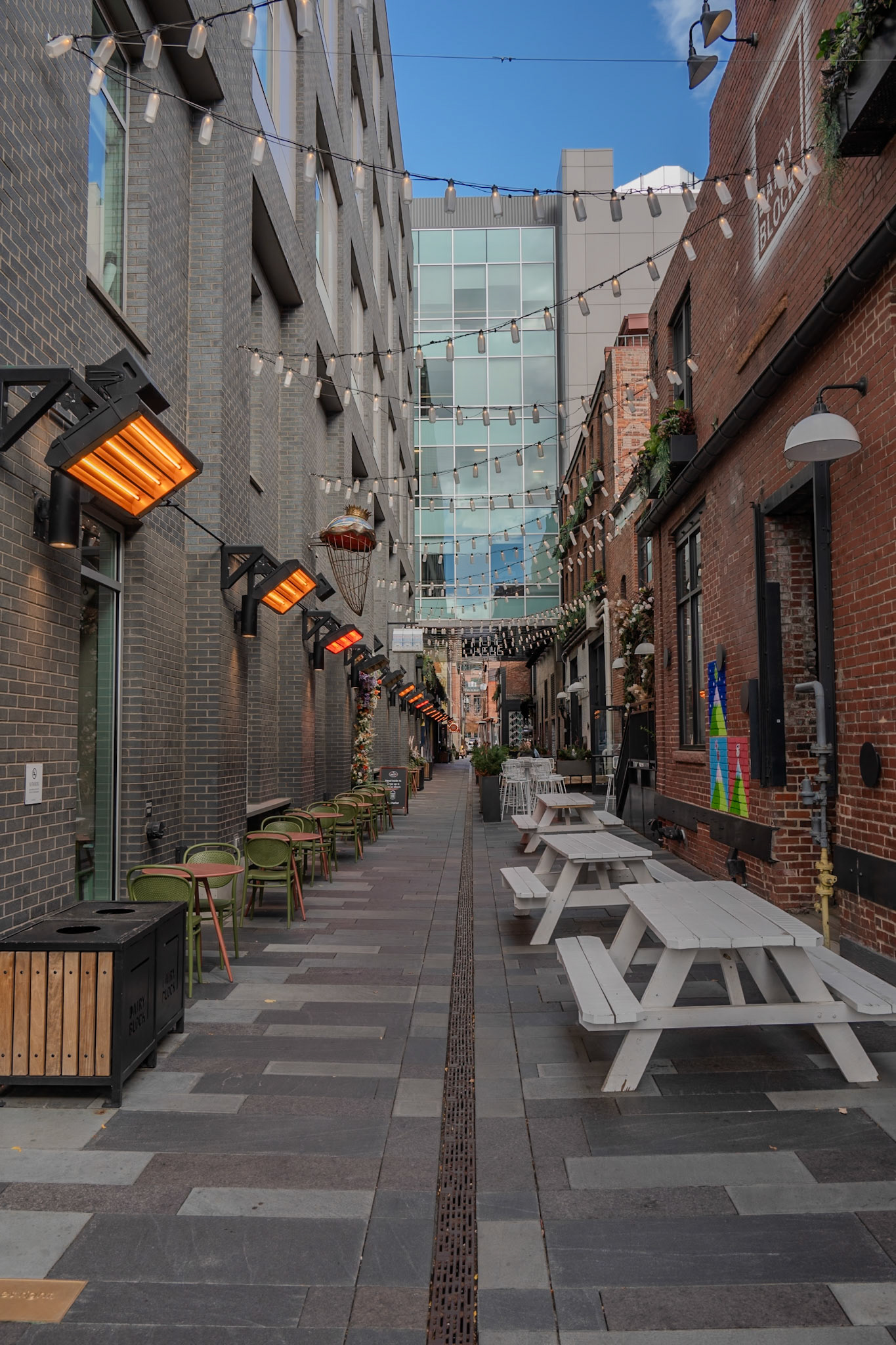 A charming urban alley adorned with string lights and outdoor seating. The vibrant mix of modern and historic architecture creates a cozy and inviting atmosphere in this bustling city location.