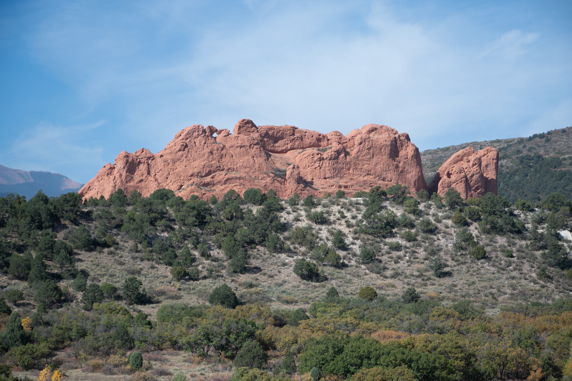 A breathtaking red rock formation stands prominently against a clear blue sky, surrounded by lush greenery. This natural landscape captivates with its rugged beauty and serene atmosphere.
