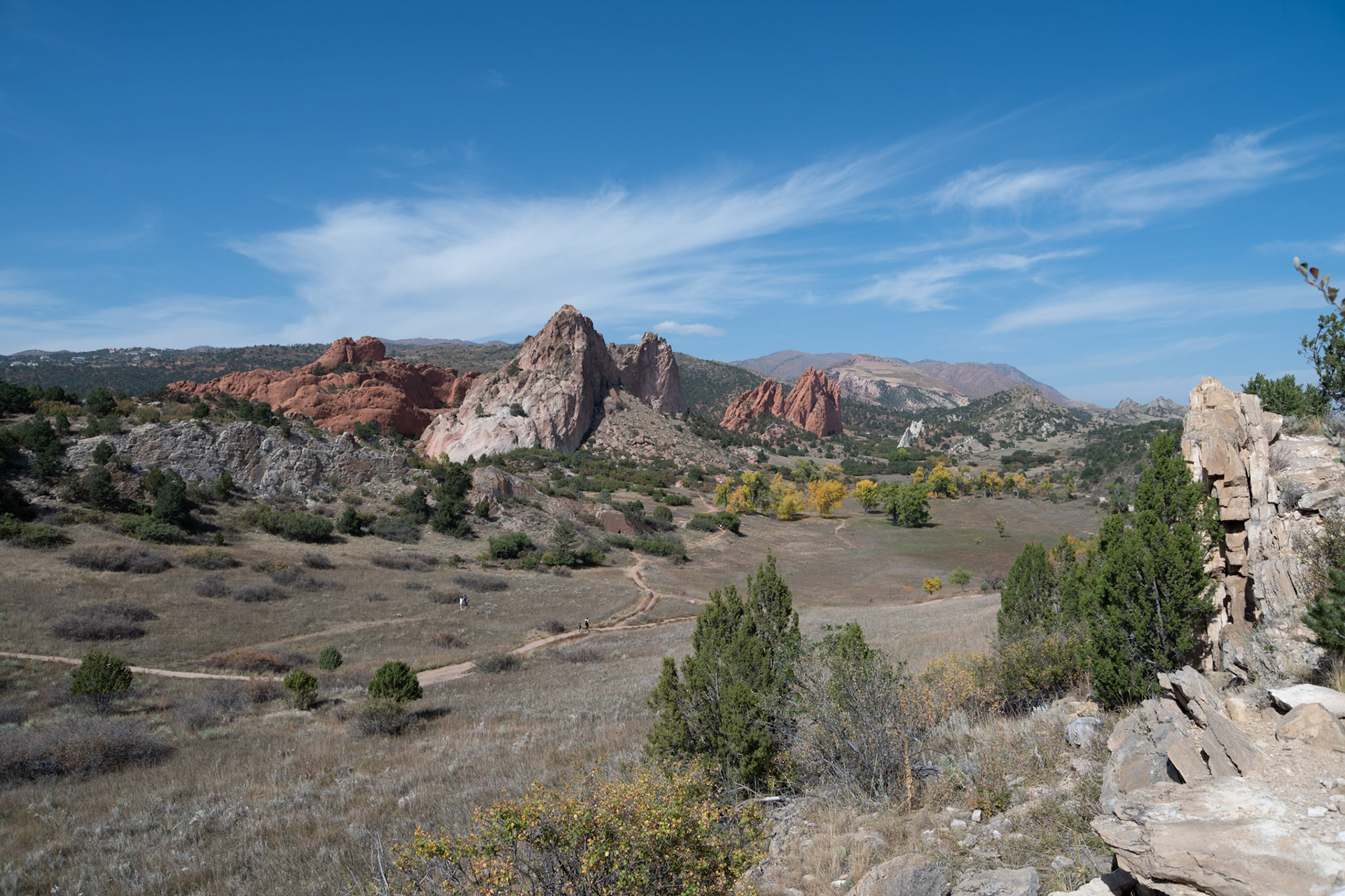 A breathtaking view of red rock formations under a vibrant blue sky. The arid landscape is complemented by scattered greenery, creating a serene natural scene perfect for outdoor enthusiasts and nature lovers.