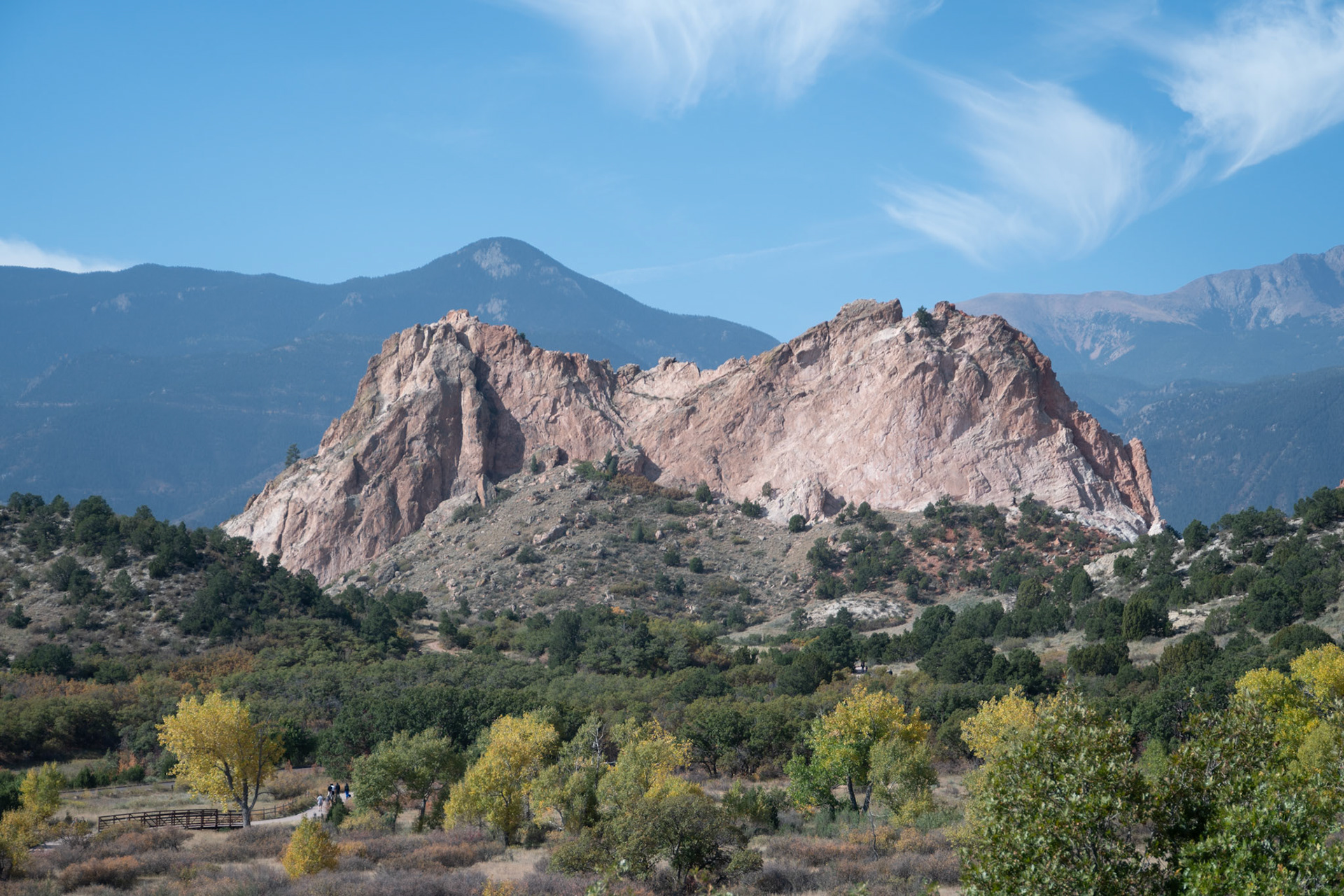 This image captures striking red rock formations surrounded by lush greenery and mountains under a vibrant blue sky, offering a peaceful and scenic nature scene.