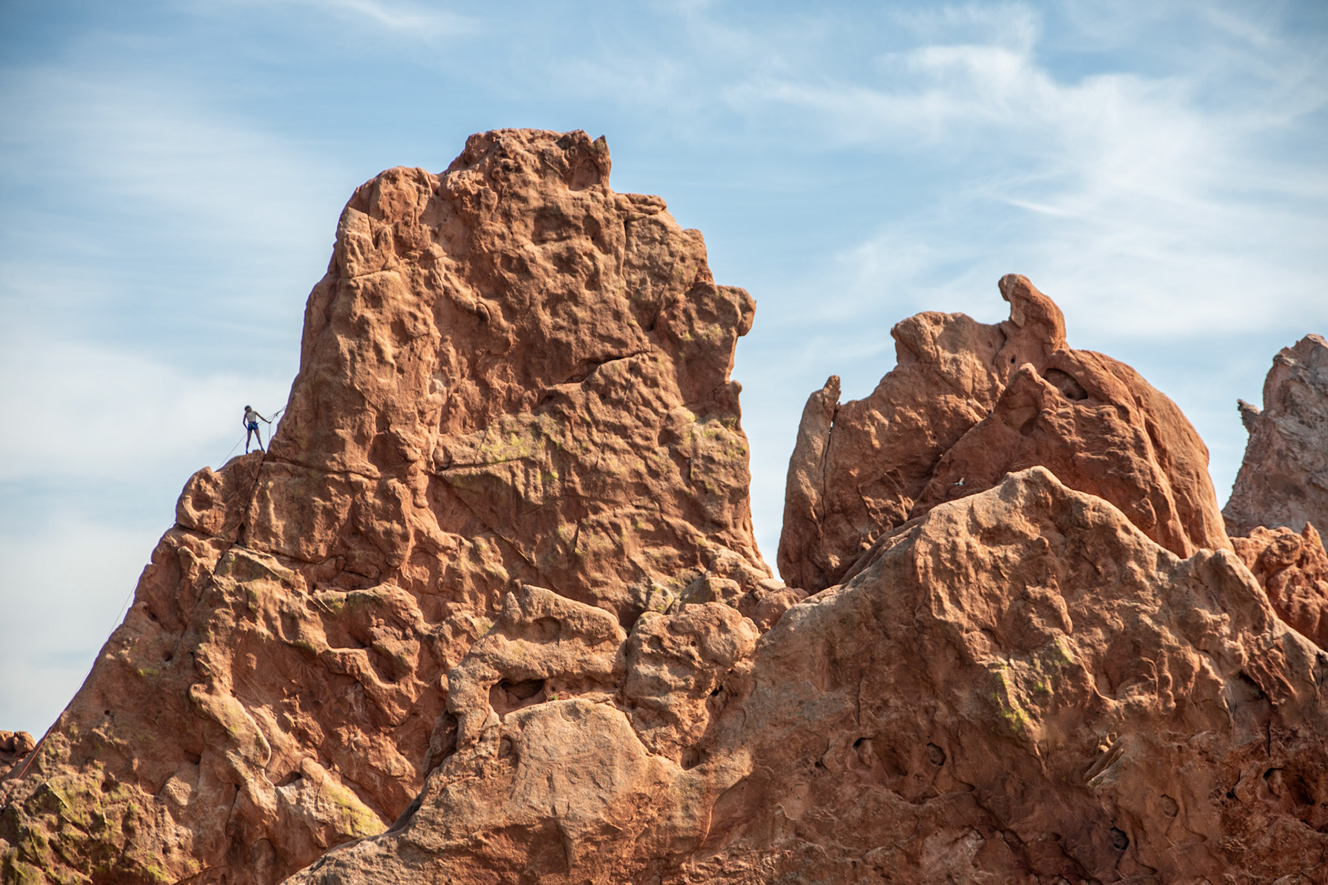 A lone climber scales a dramatic rocky cliff, showcasing determination and adventure, against a backdrop of clear blue skies. The scene captures the thrill and challenge of rock climbing.