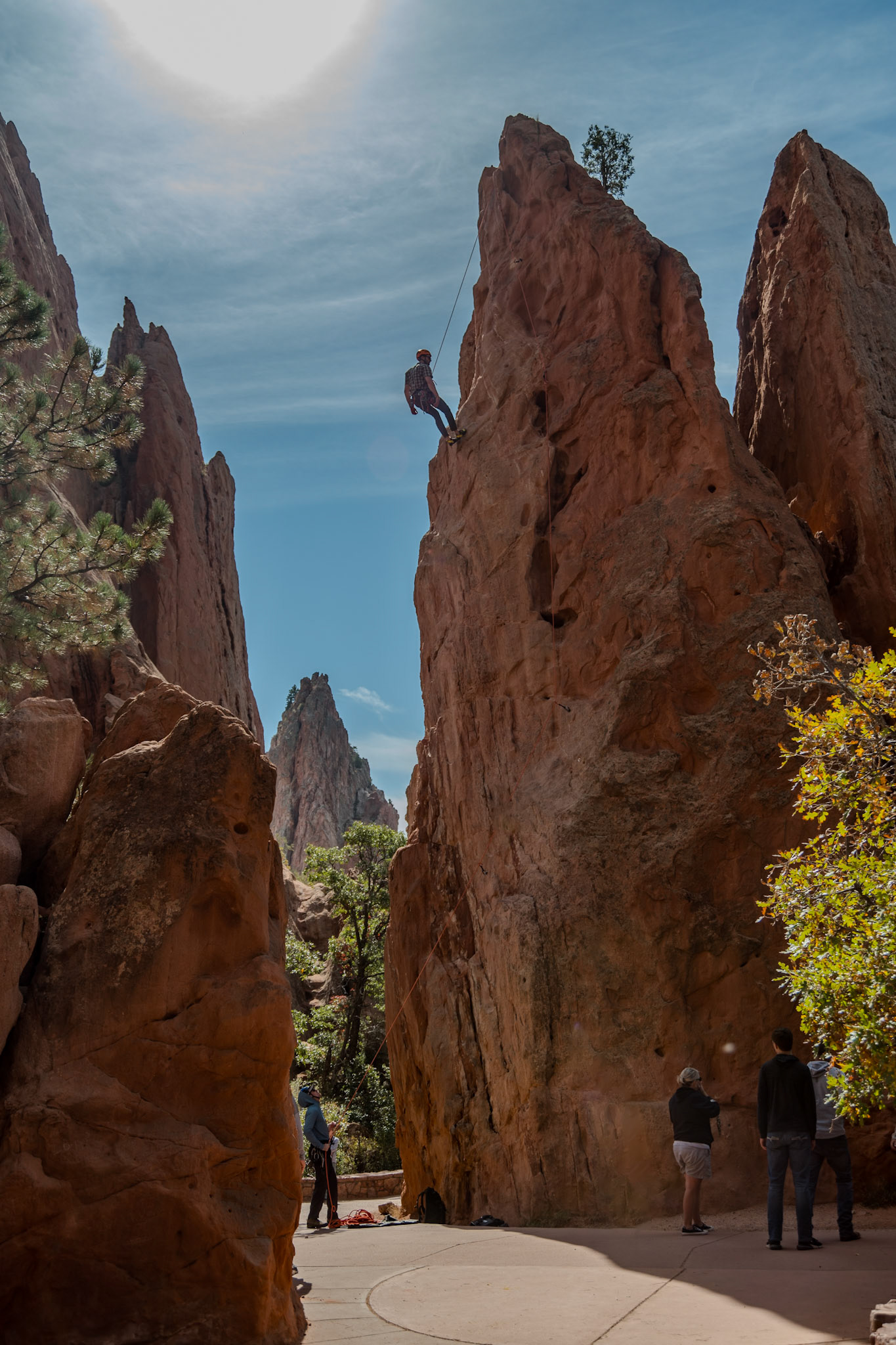 An explorer in a helmet ascends steep rock formations, surrounded by awe-inspiring natural scenery under a bright blue sky, representing courage and adventure in nature.