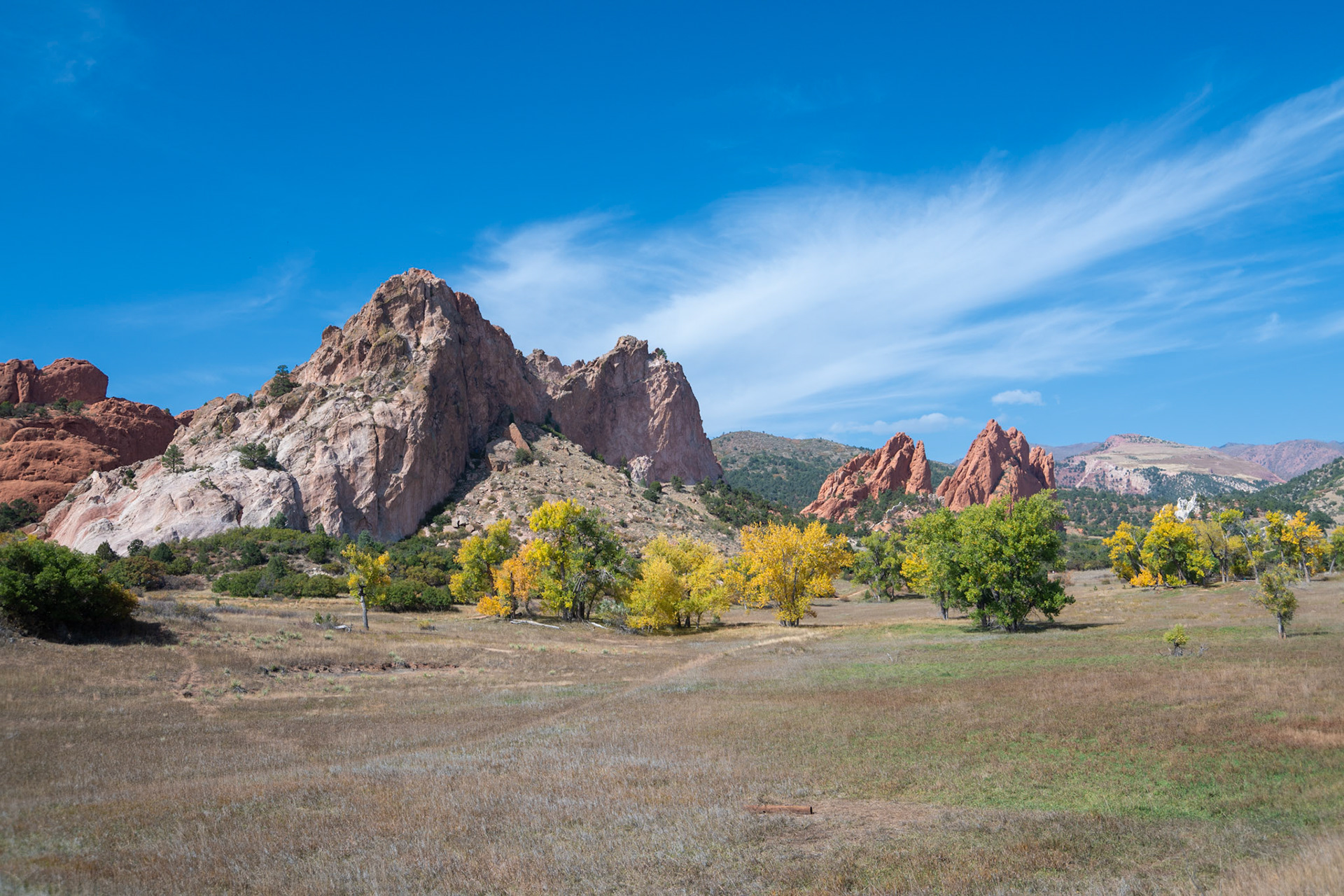A stunning view of rocky mountains surrounded by colorful autumn trees under a bright blue sky, capturing the essence of peace and natural beauty in the wilderness.