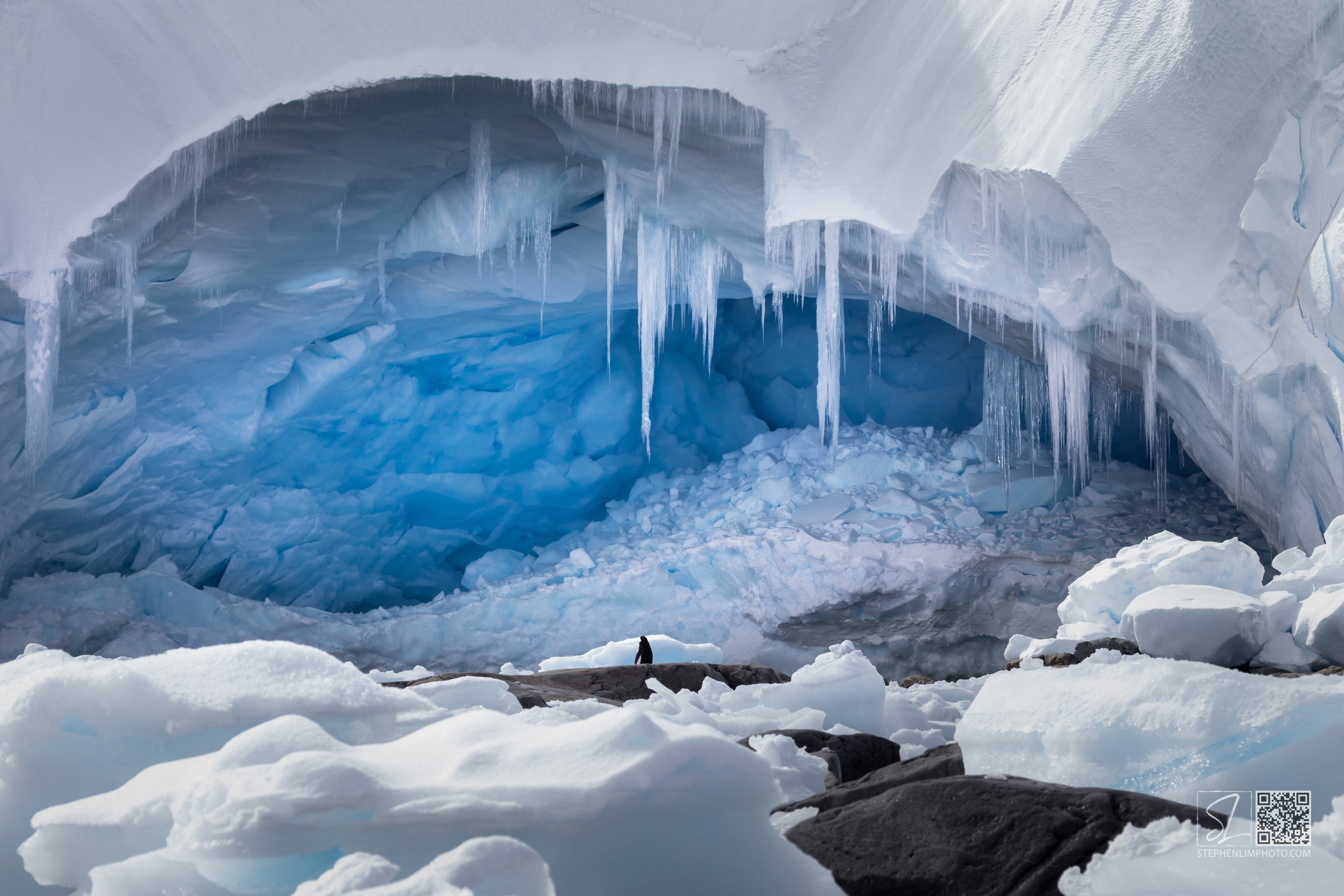 Trapping the Sky in Ice:  A lone penguin peers at an enormous ice cave in Antarctica