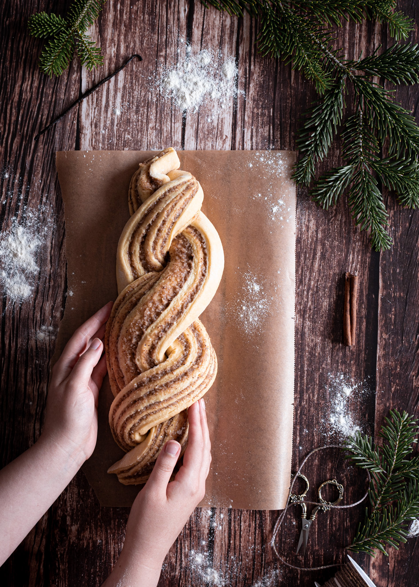 hazelnut babka on parchment paper, pine branches, cinnamon, vanilla, wooden table