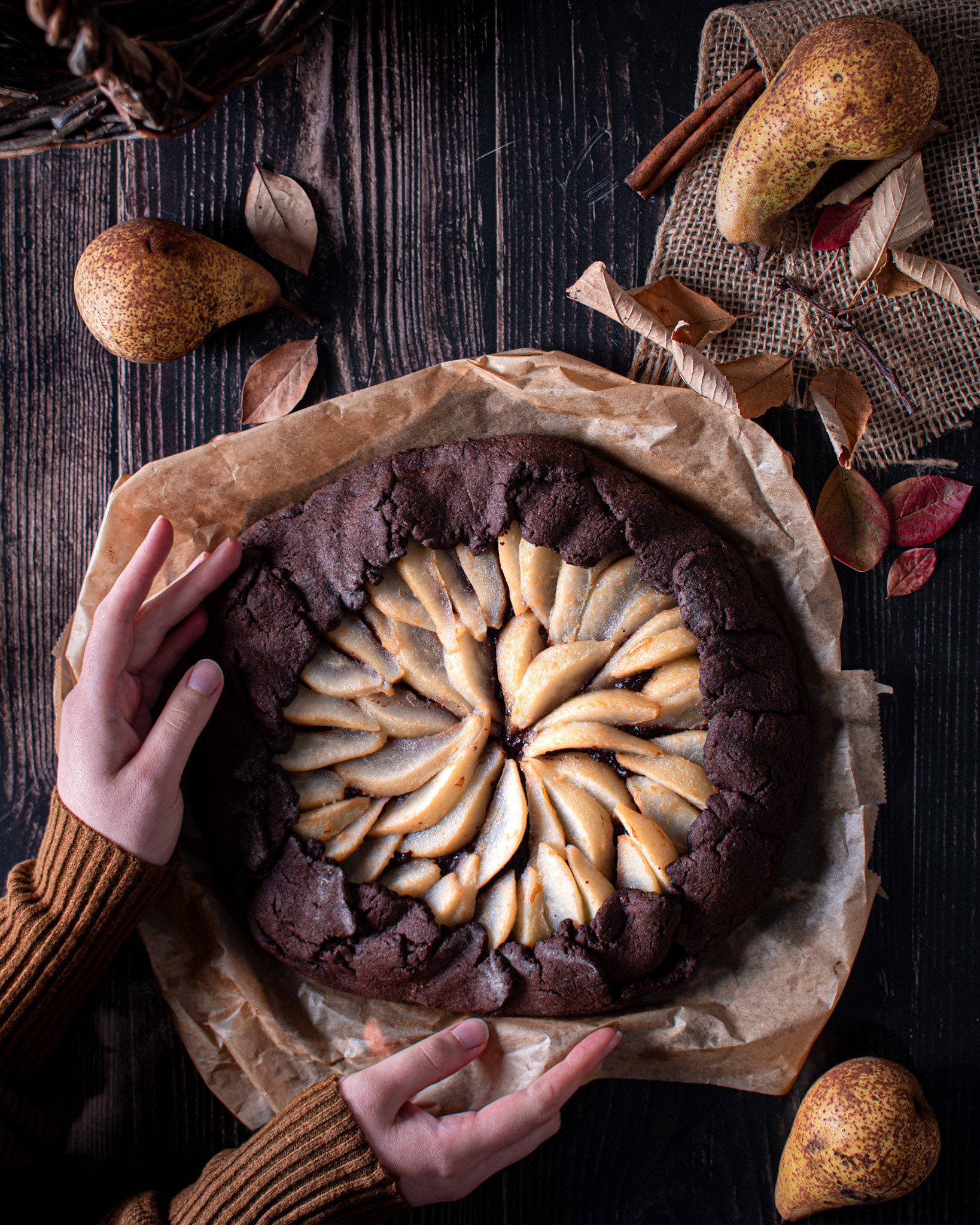 chocolate pear galette on wooden board with pears, cinnamon stick and fall leaves