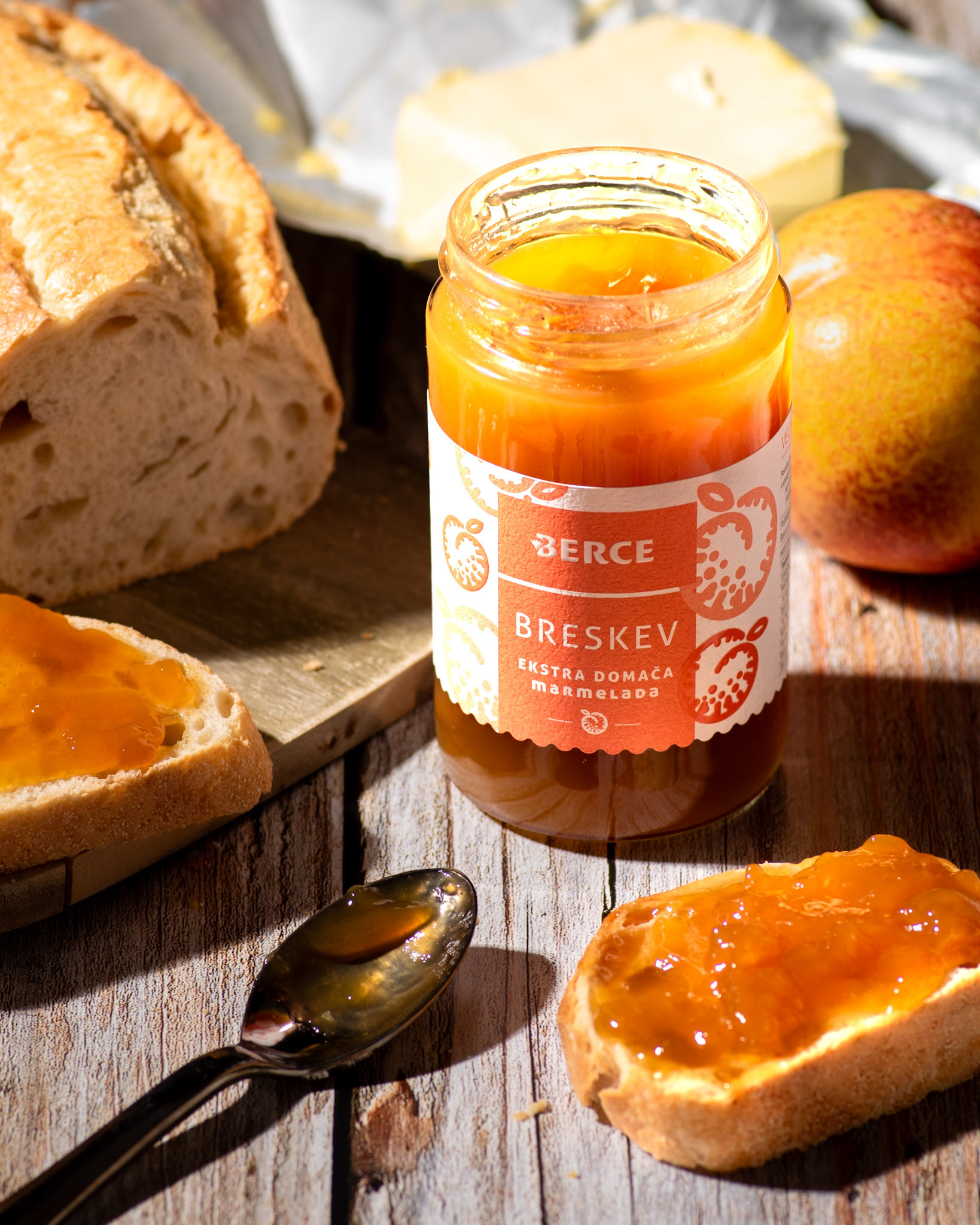peach jam in a jar and on bread, spoon, peach, bread and butter on sunlight