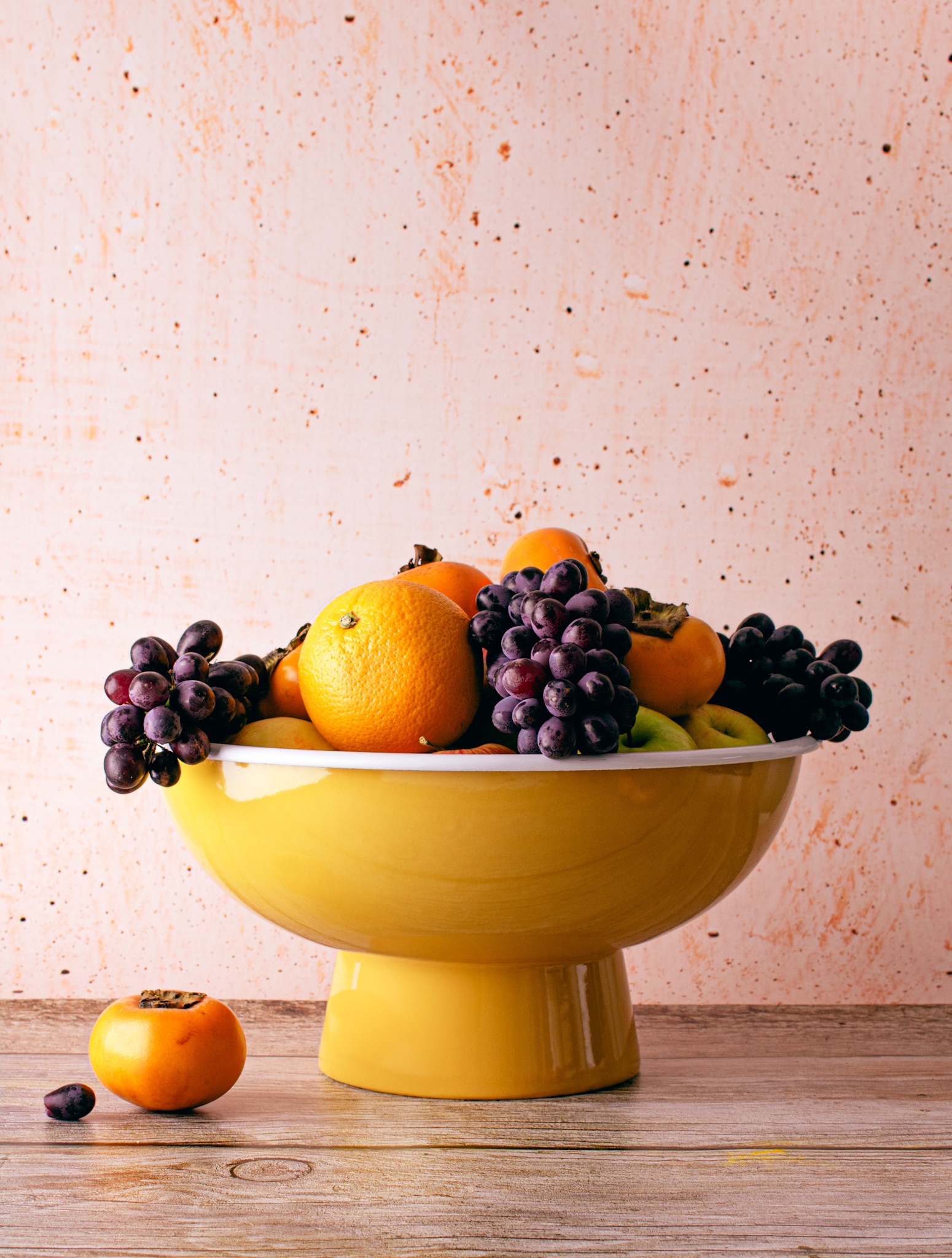 yellow fruit bowl with orange, grapes and persimmon