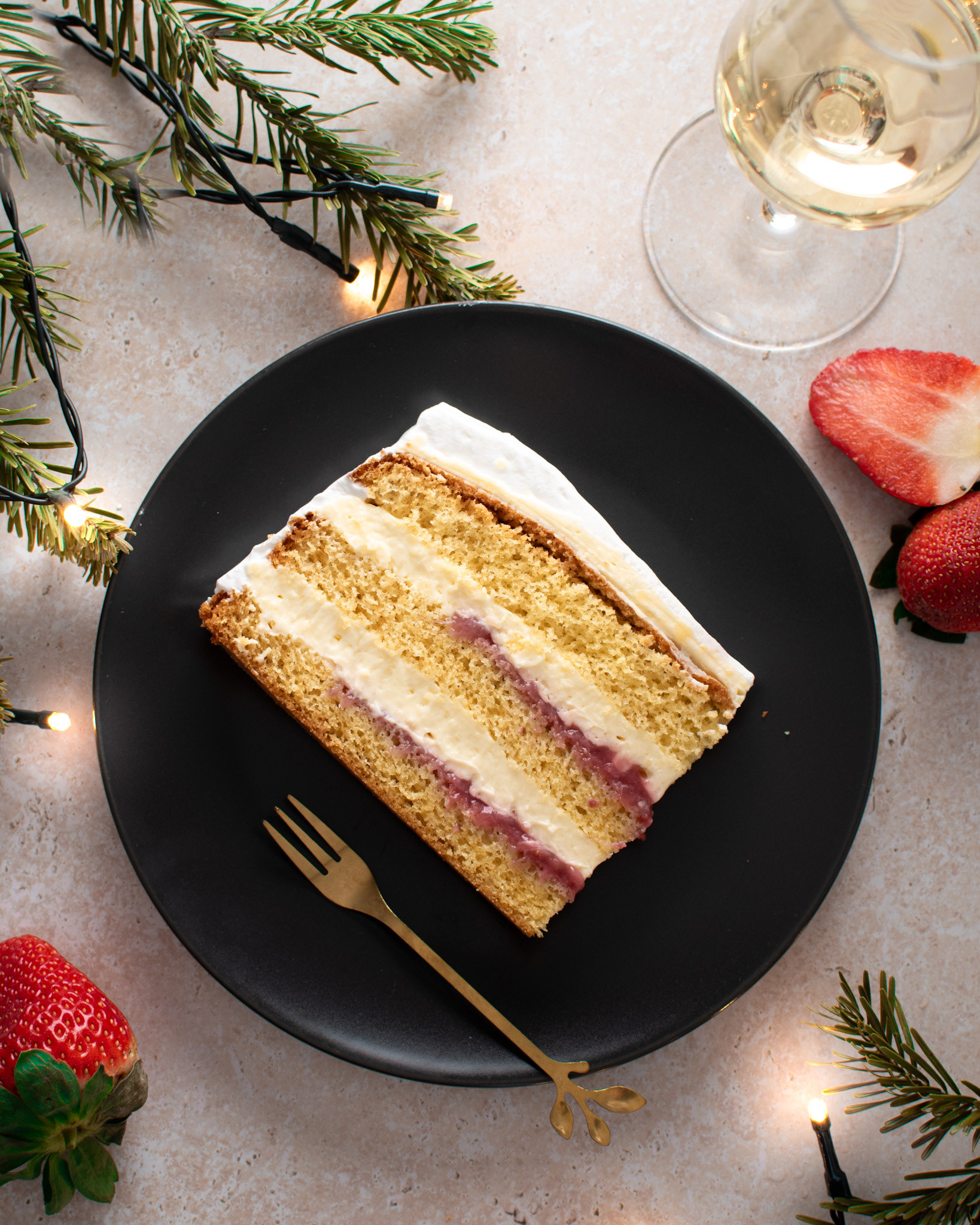vanilla layer cake, strawberries, glass of champagne, christmas lights, pine tree branches