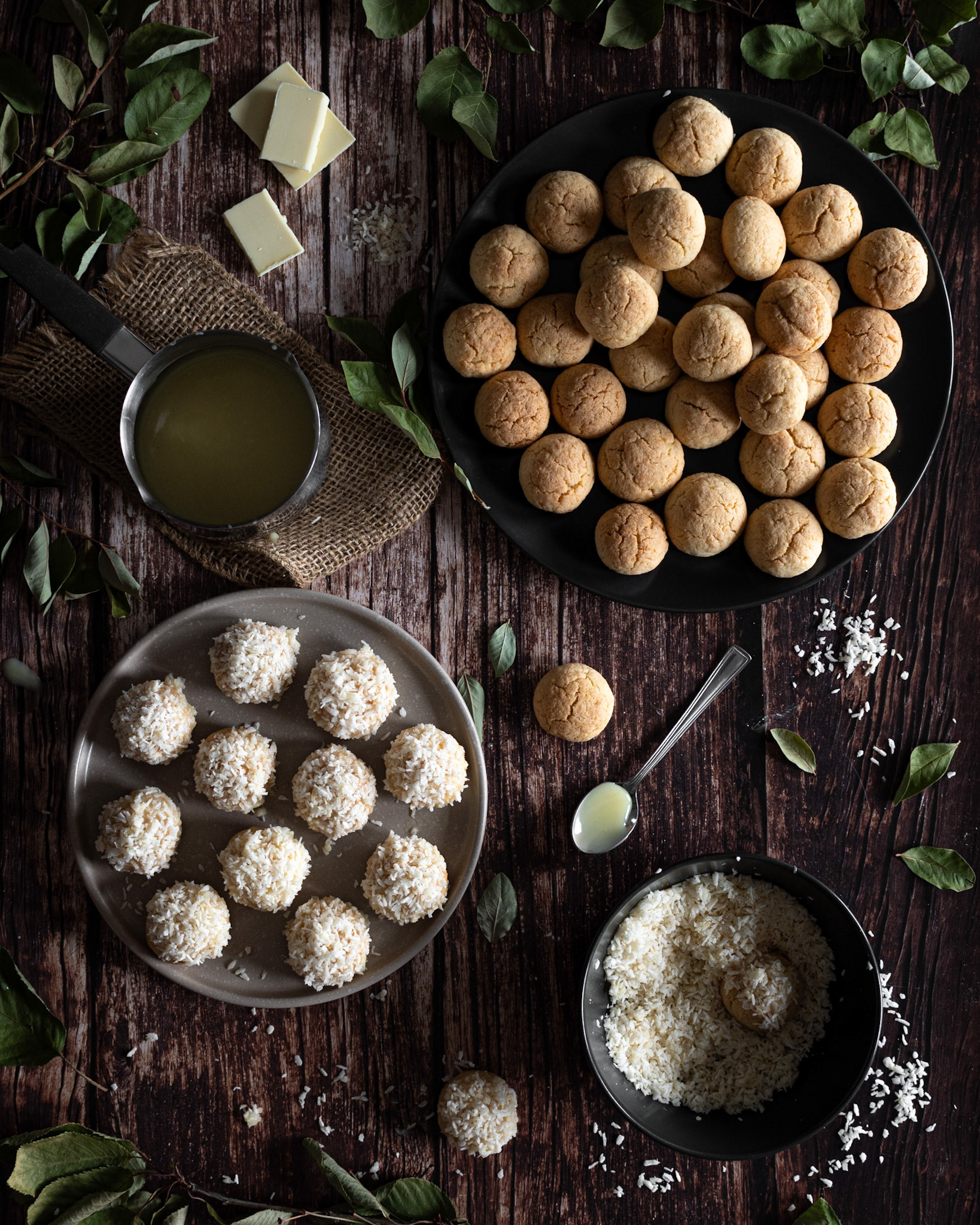 coconut cookies being prepared with white chocolate and shredded coconut on a dark wooden table with greenery