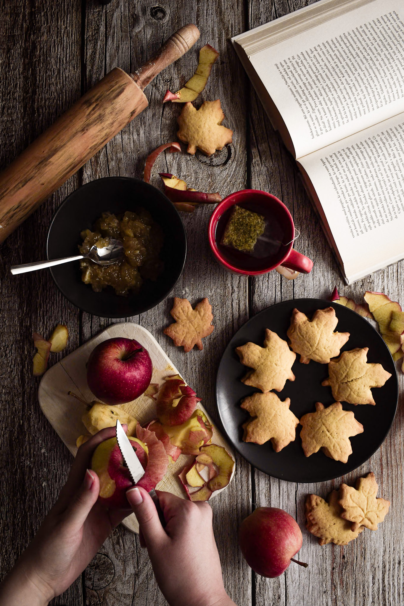 apple cookies in shapes of leaves, hands peeling an apple, tea and a book