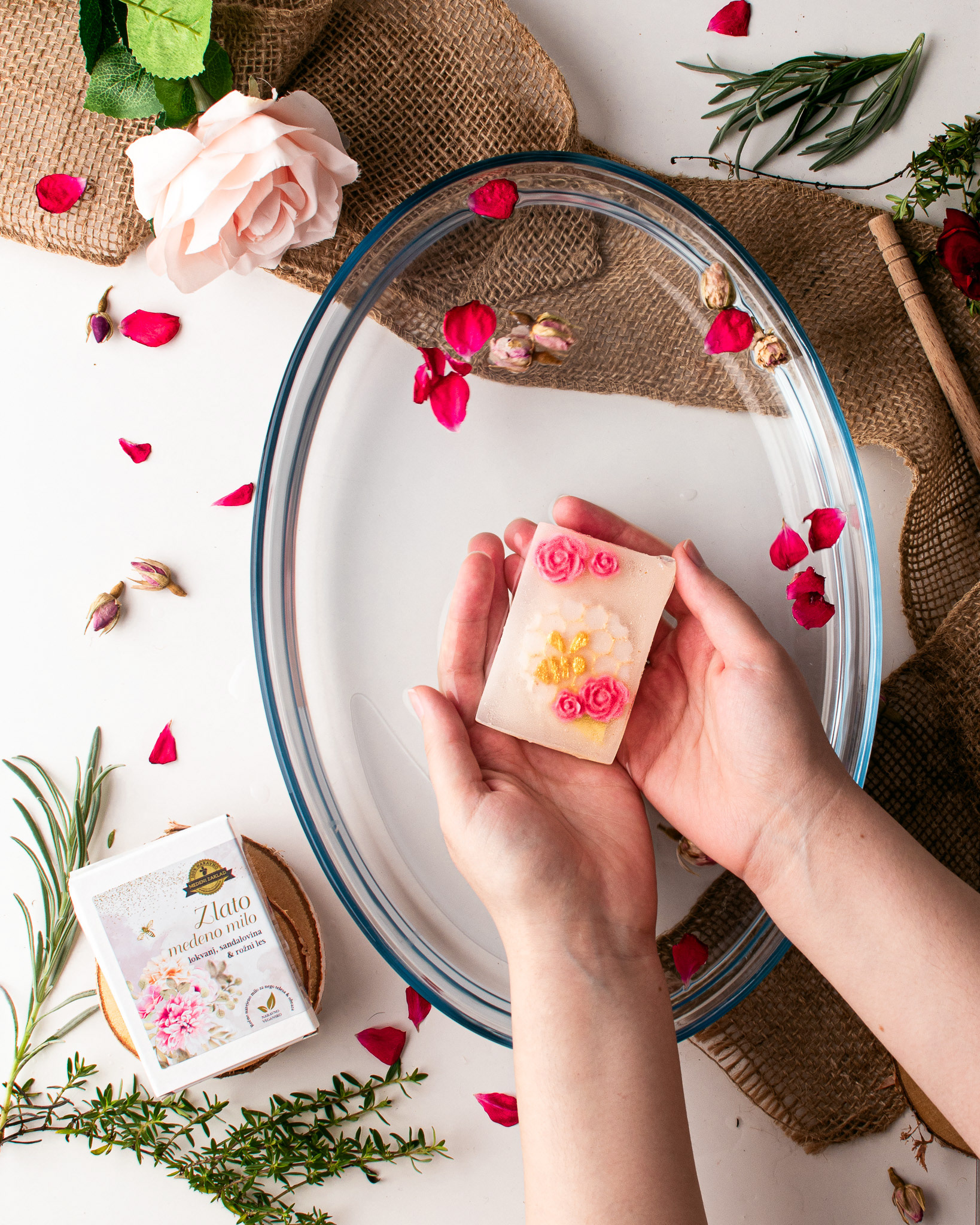 Hands holding a flowery soap, rose leaves, herbs and roses