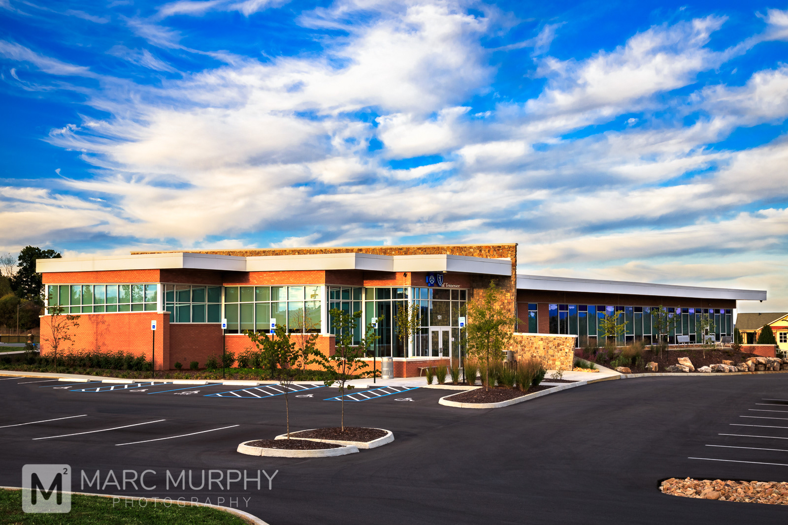 Exterior Single Story Blue Cross Blue Shield Brick and Glass Office Building at Sunset with Parking Lot, White Clouds and Blue Sky