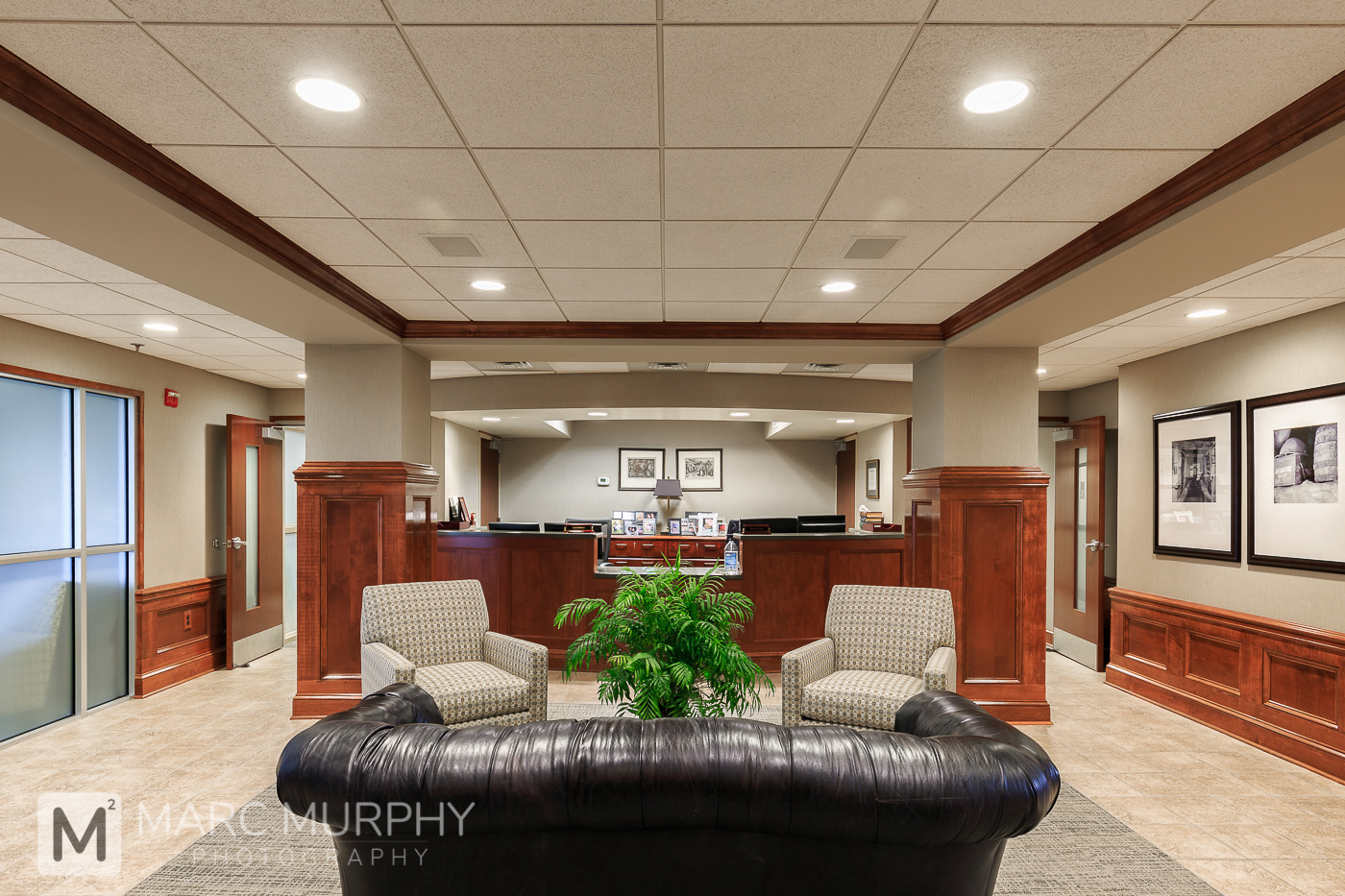 Corporate Office Waiting Room Reception Area with Receptionist Desk, Black Leather Couch Tan Chairs and Wood Wainscoting on Wall