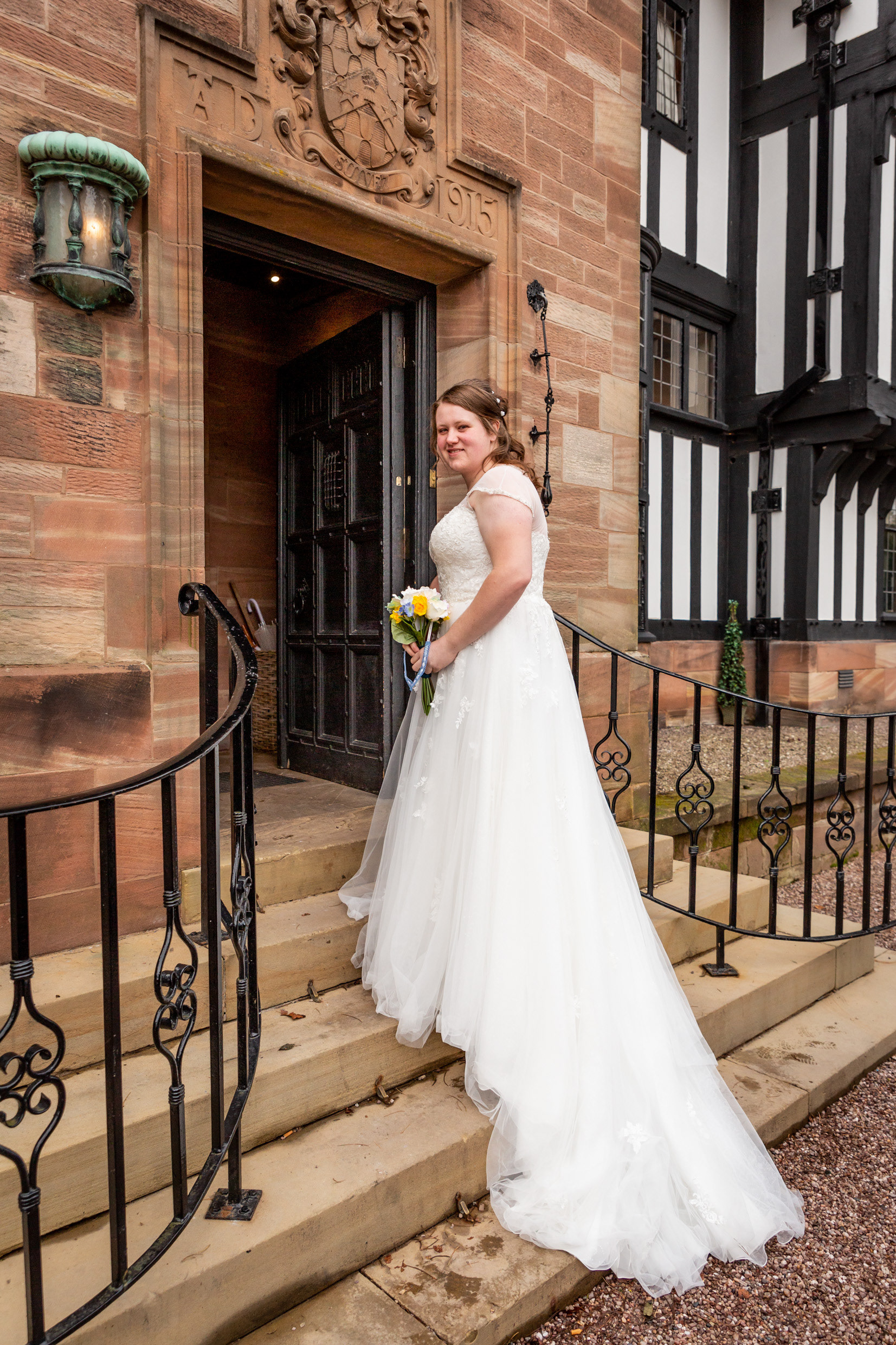A bride in a white wedding dress looks back over her shoulder as she walks up the steps into Inglewood Manor on her wedding day.
