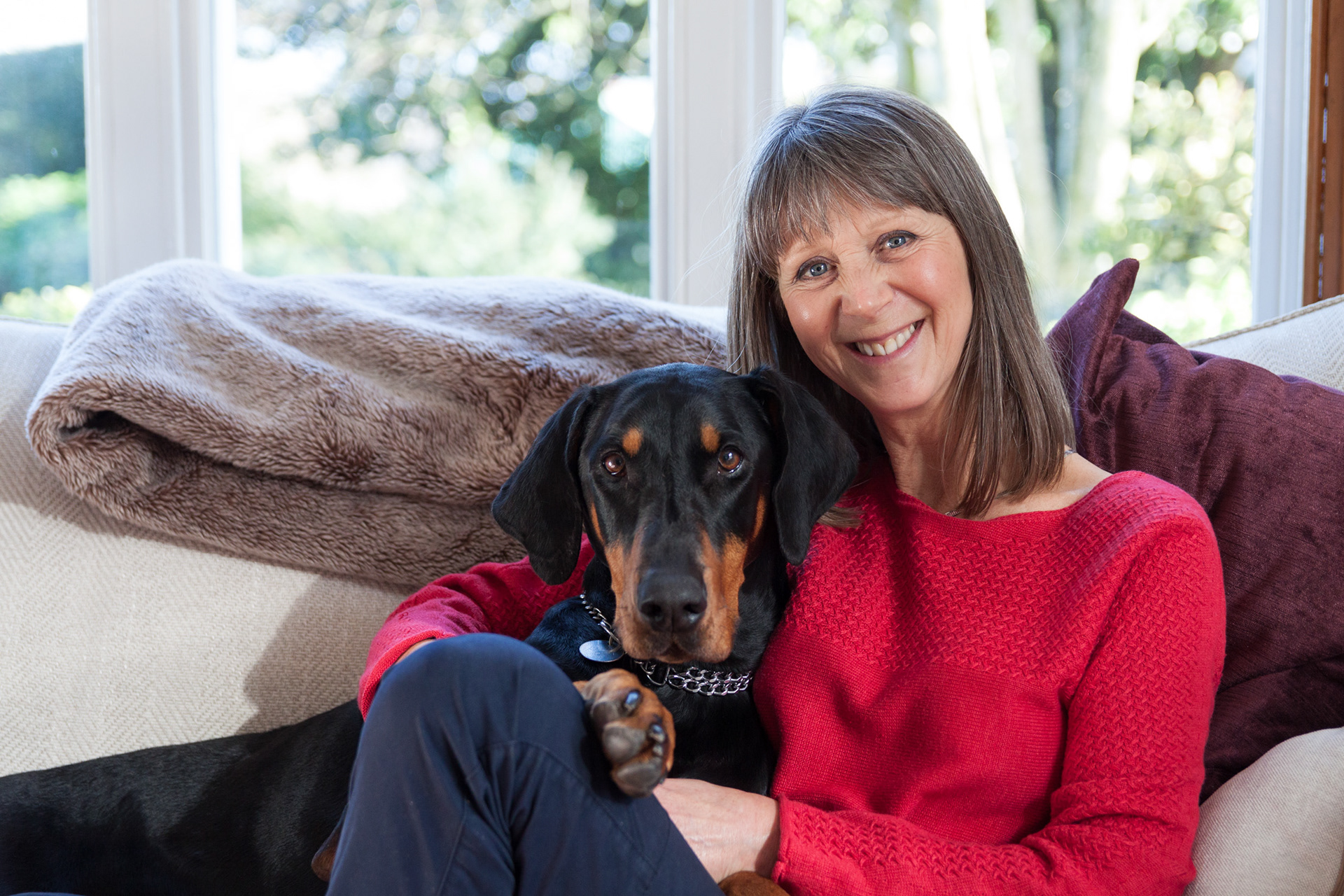 Portrait Photography. A lady cuddles up to her dog (a Doberman) on the sofa.