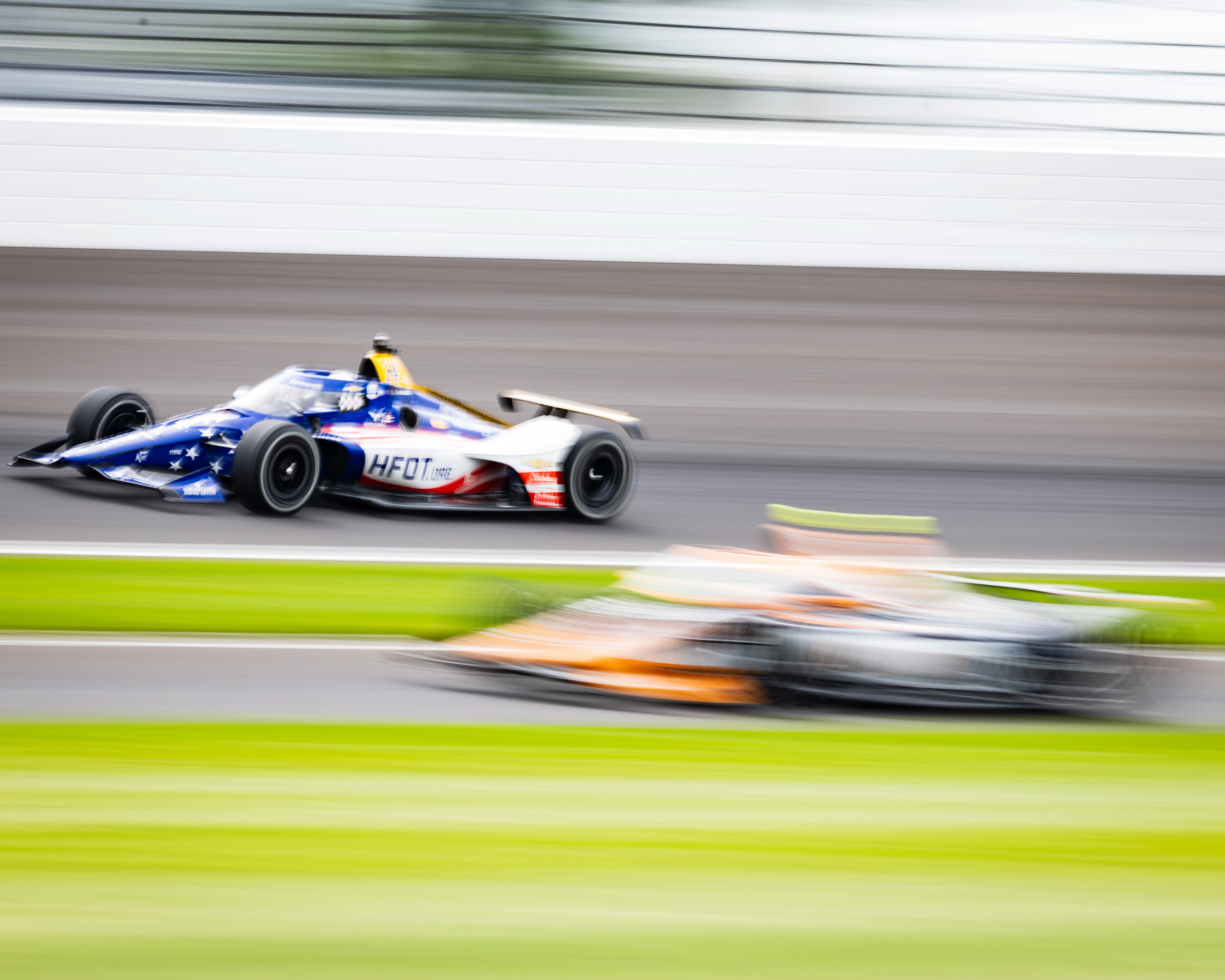 Santino Ferrucci, driver of the No. 14 Chevrolet for A.J. Foyt Enterprises (left), rounds Turn 2 as Romain Grosjean, driver of the No. 18 Honda for Dale Coyne Racing, exits the pit lane during Carb Day practice of the 110th Indianapolis 500, located in Speedway, Indiana, on May 22, 2026. 