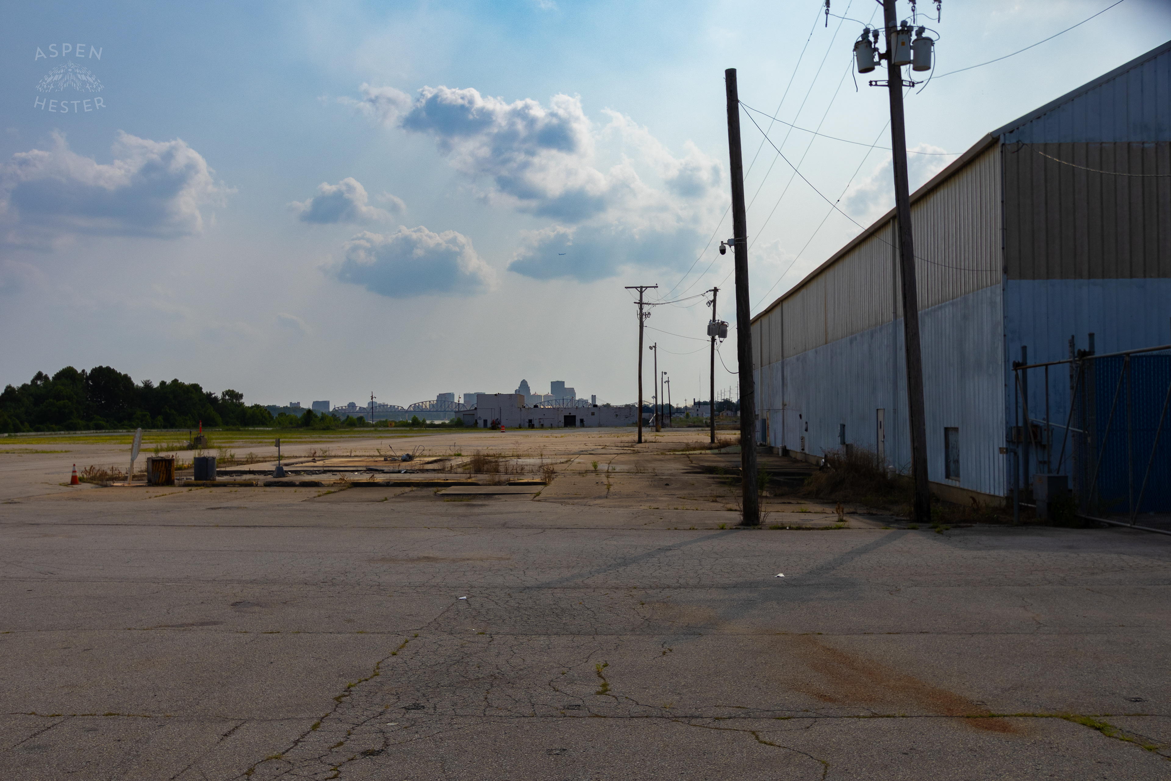 Looking Through the Chain Link Fence Towards the Louisville Skyline at the Abandoned Jeffboat Shipyard. July 26th, 2024/Aspen Hester