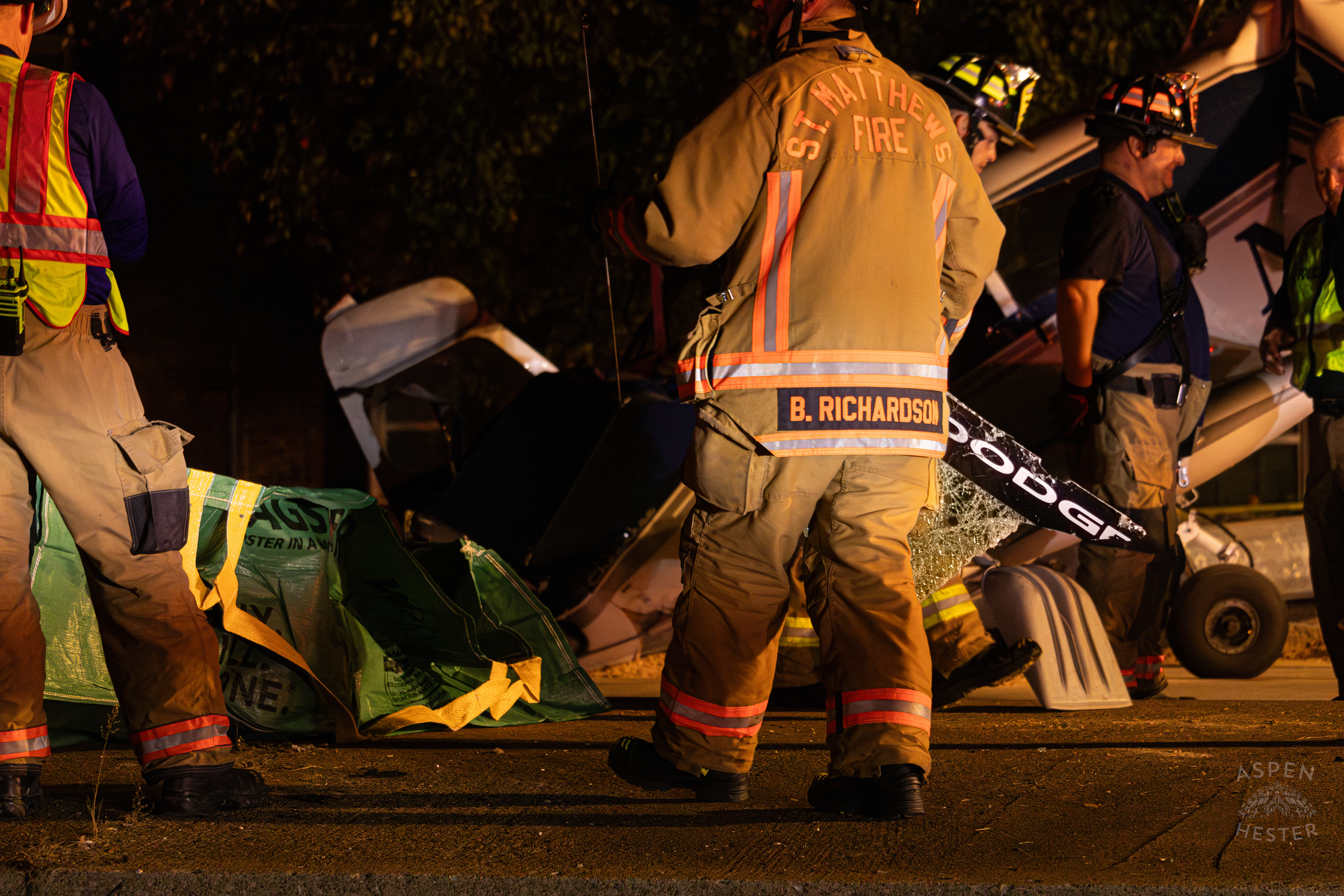 St. Matthews Firefighter Carrying A Piece of The Shattered Dodge Charger’s Windshield to The Debris Pile so A Crew from Tony’s Wreckers Can Begin Removing The Piper Cherokee Plane from the Road after it Crash Landed, Taking Out Utility Poles, and Hitting A Car on Breckenridge Lane and Kresge Way. October 11th, 2024/Aspen Hester 