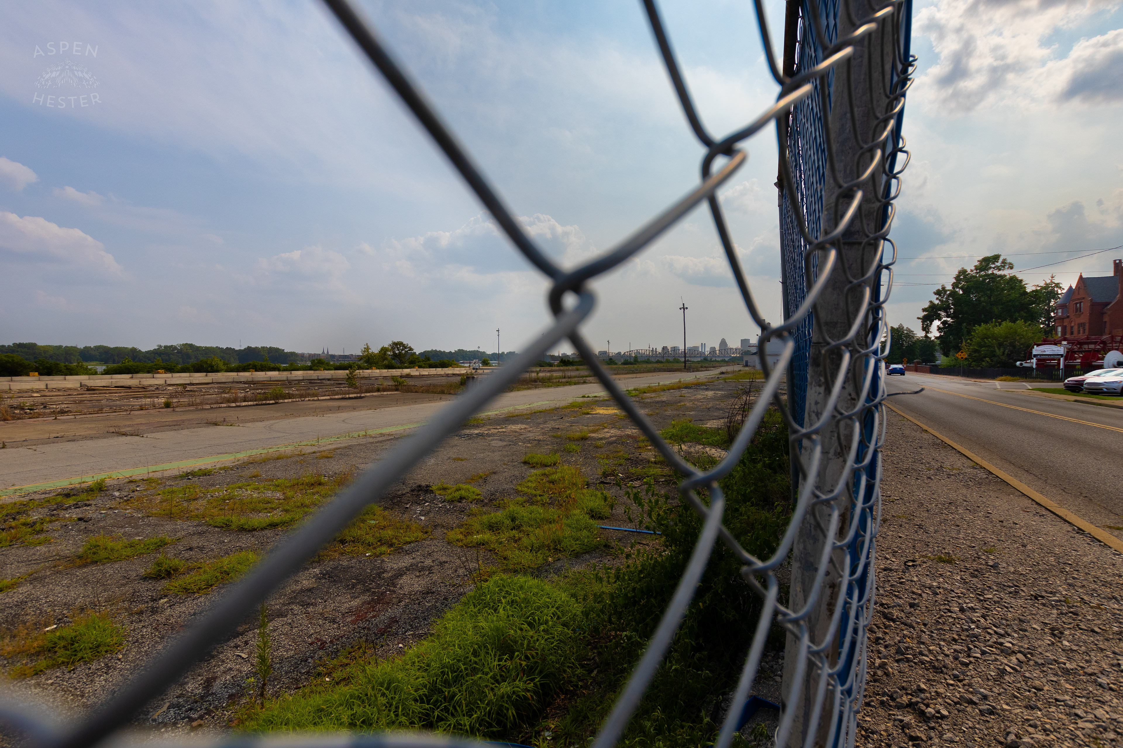 Looking Through the Chain Link Fence Towards the Louisville Skyline at the Abandoned Jeffboat Shipyard. July 26th, 2024/Aspen Hester