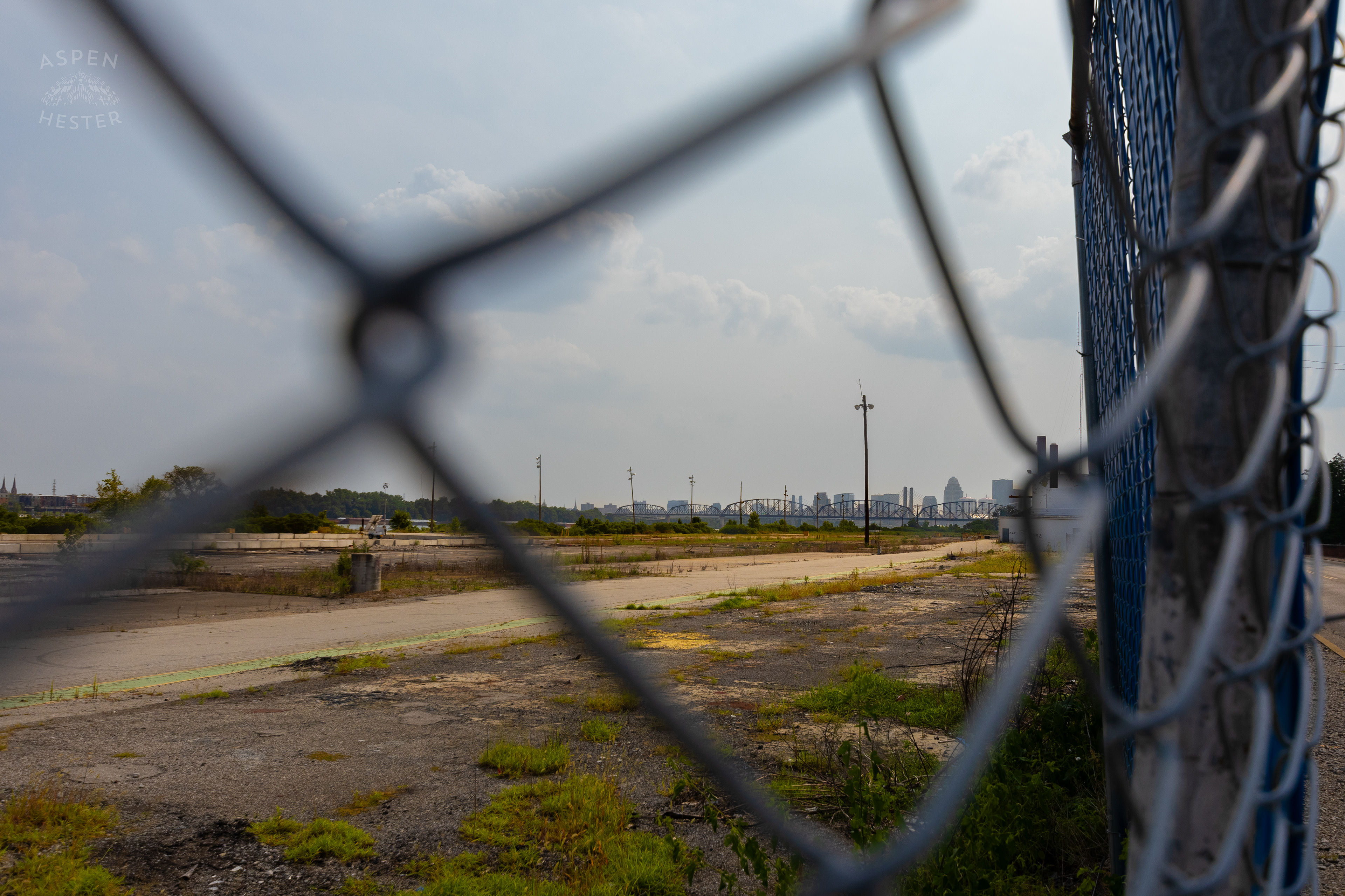 Looking Through the Chain Link Fence Towards the Louisville Skyline at the Abandoned Jeffboat Shipyard. July 26th, 2024/Aspen Hester