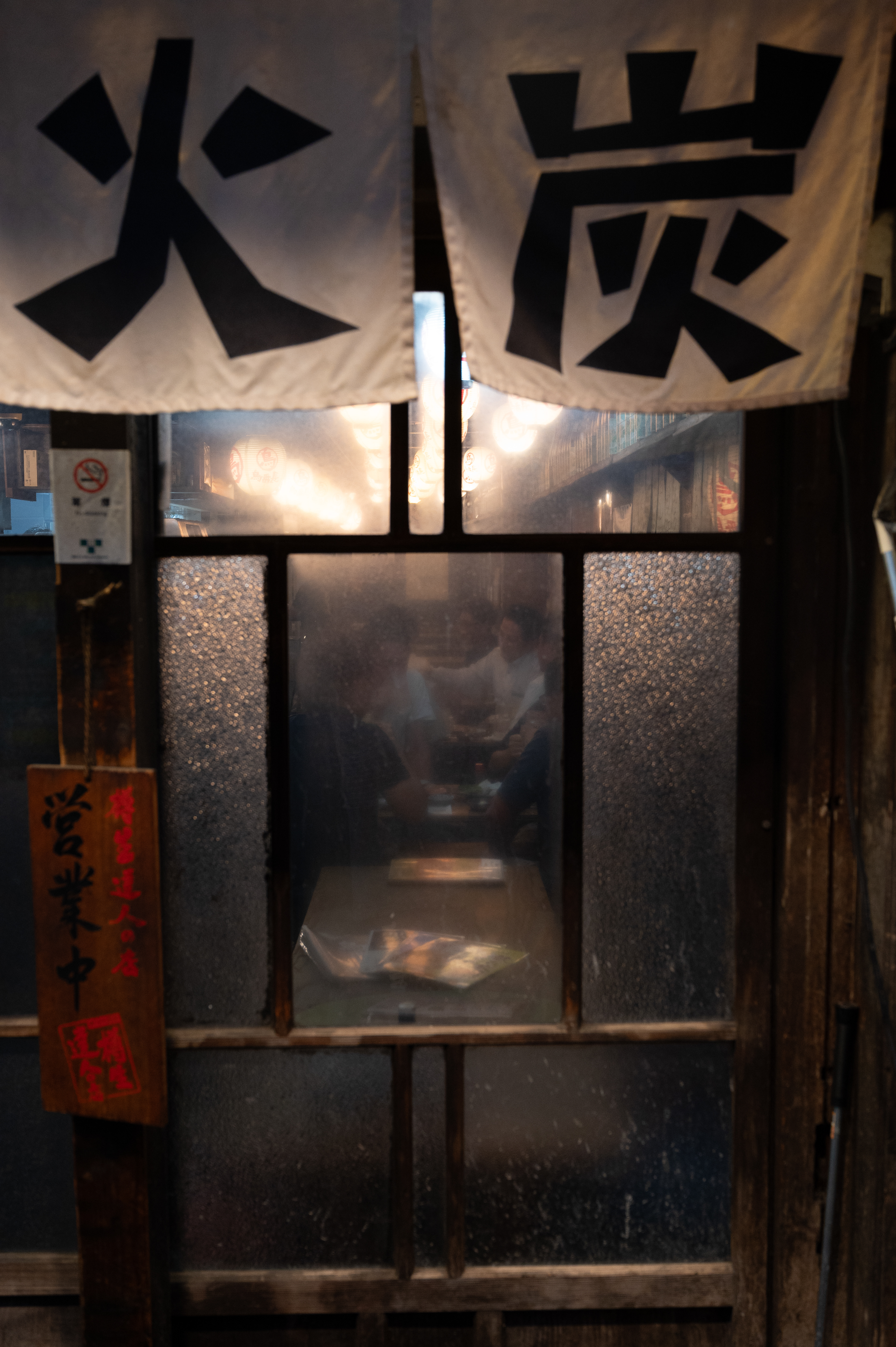 A peek into a cozy, traditional eatery through frosted glass doors, illuminated warmly, with subtle signs of life and activity inside.