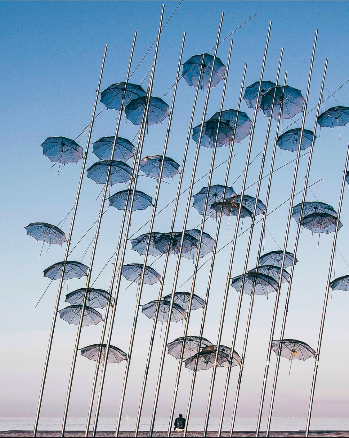 The iconic umbrella installation on a clear day, with a lone individual sitting beneath, symbolizing tranquility and creativity.