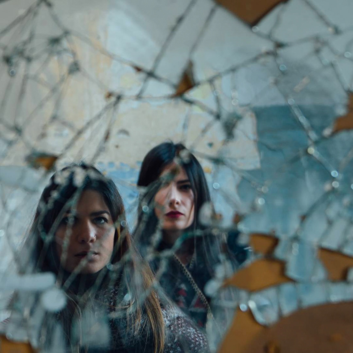Two women with serious expressions captured through the fragmented and reflective surface of broken glass in an artistic composition.