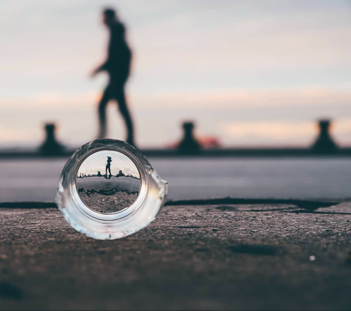 A silhouette of a person walking in the background captured through a glass sphere, reflecting the scene upside-down on a concrete surface.